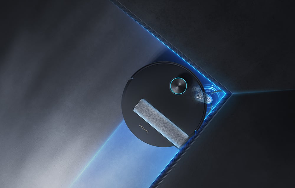 Egy fekete robot porszívó szürke felmosó párnával. Egy sarokban van, kék fényekkel és DREAME felirattal.