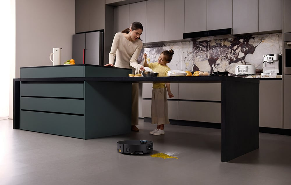 Egy nő és egy kislány süt a modern konyhában. Egy robotporszívó takarítja a kiömlött lisztet. A konyhában márvány hátfal van.