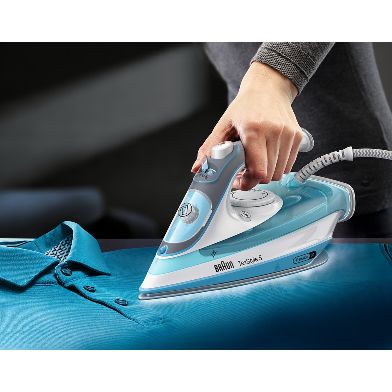 Una persona sta stirando una polo blu con un ferro da stiro blu e bianco. Il ferro è etichettato Braun TexStyle 5. Il vapore è visibile.