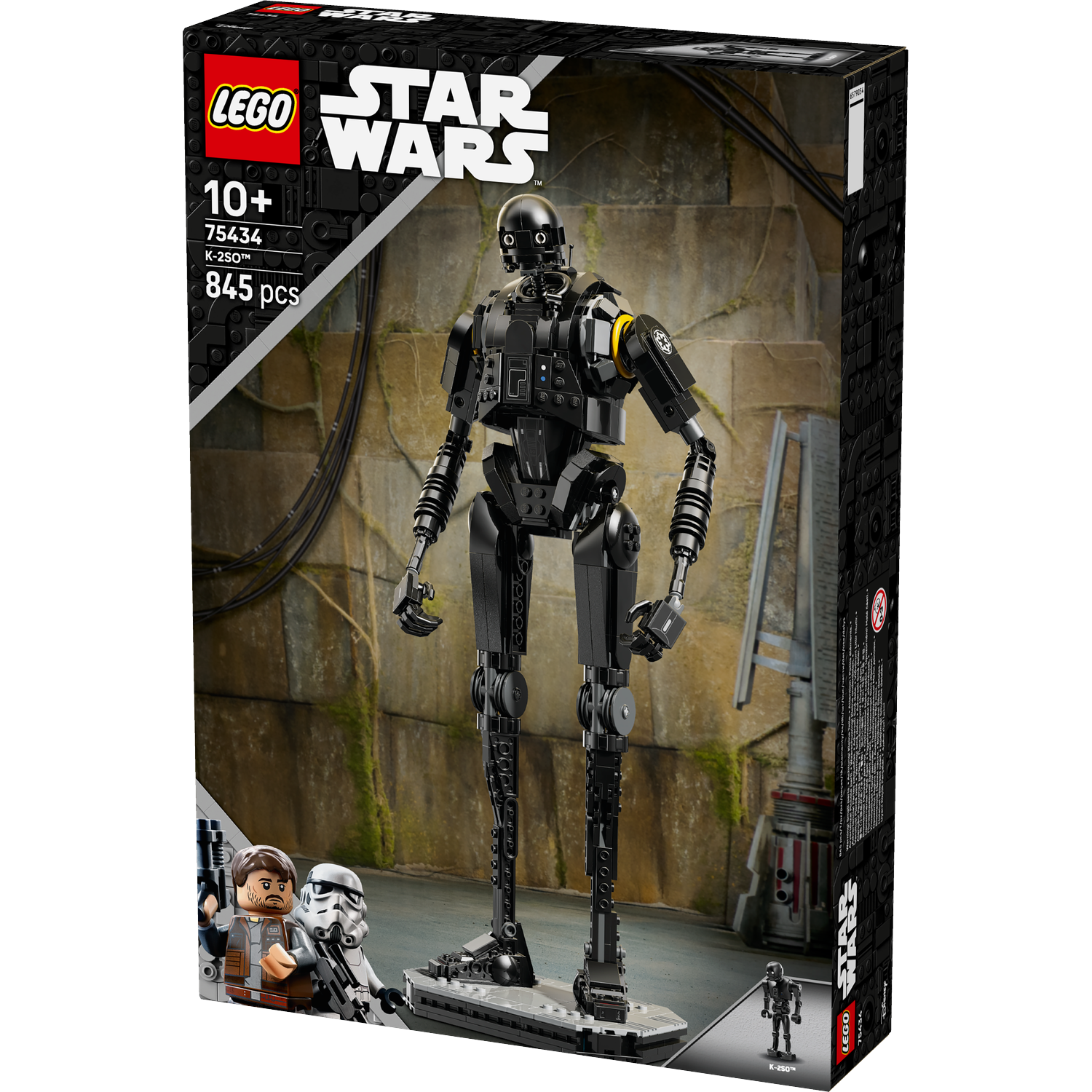 Lego Star Wars K-2SO figure on a box, black droid with yellow accent. Background shows a stone wall. Other figures at the bottom.