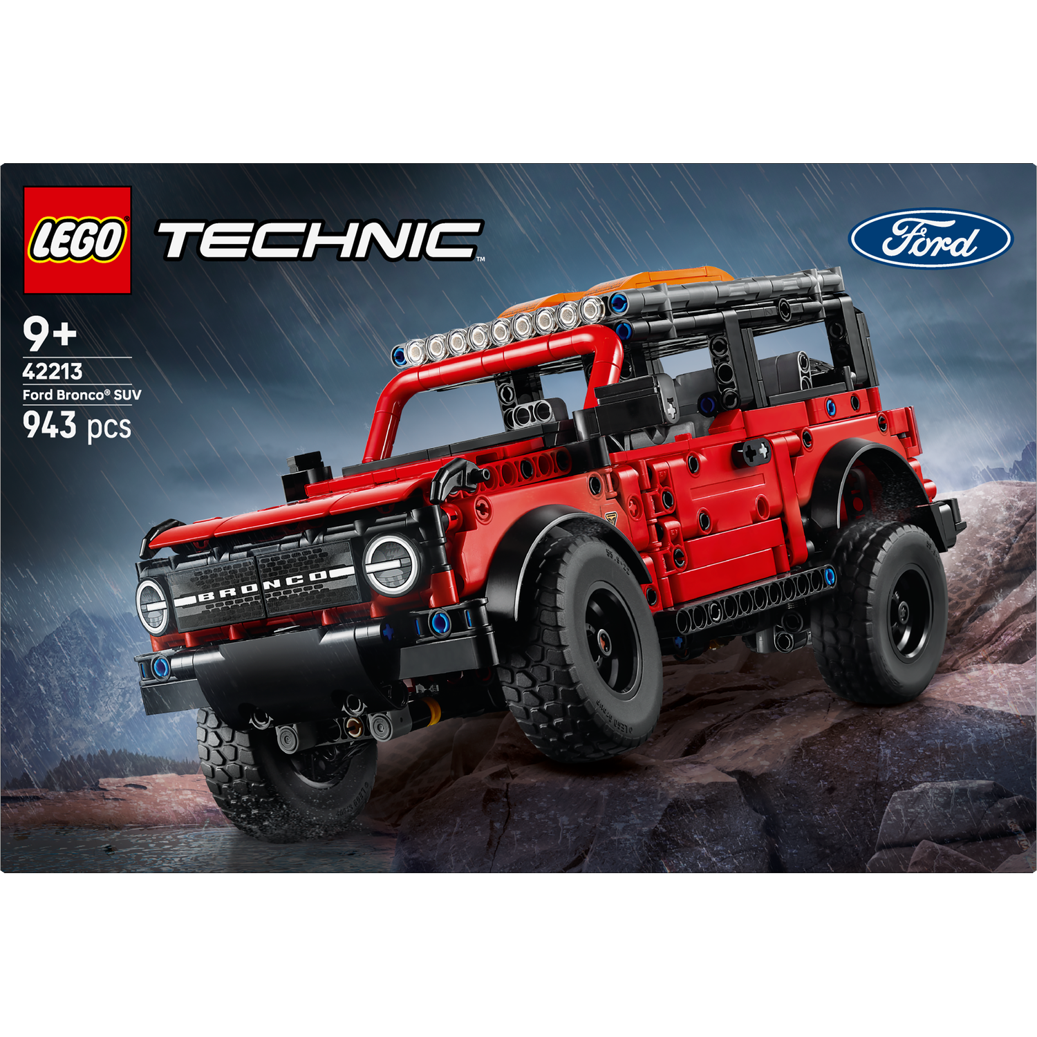 A Lego Technic Ford Bronco SUV on a rocky terrain. The red car has black wheels and a light bar. The background shows a cloudy sky.