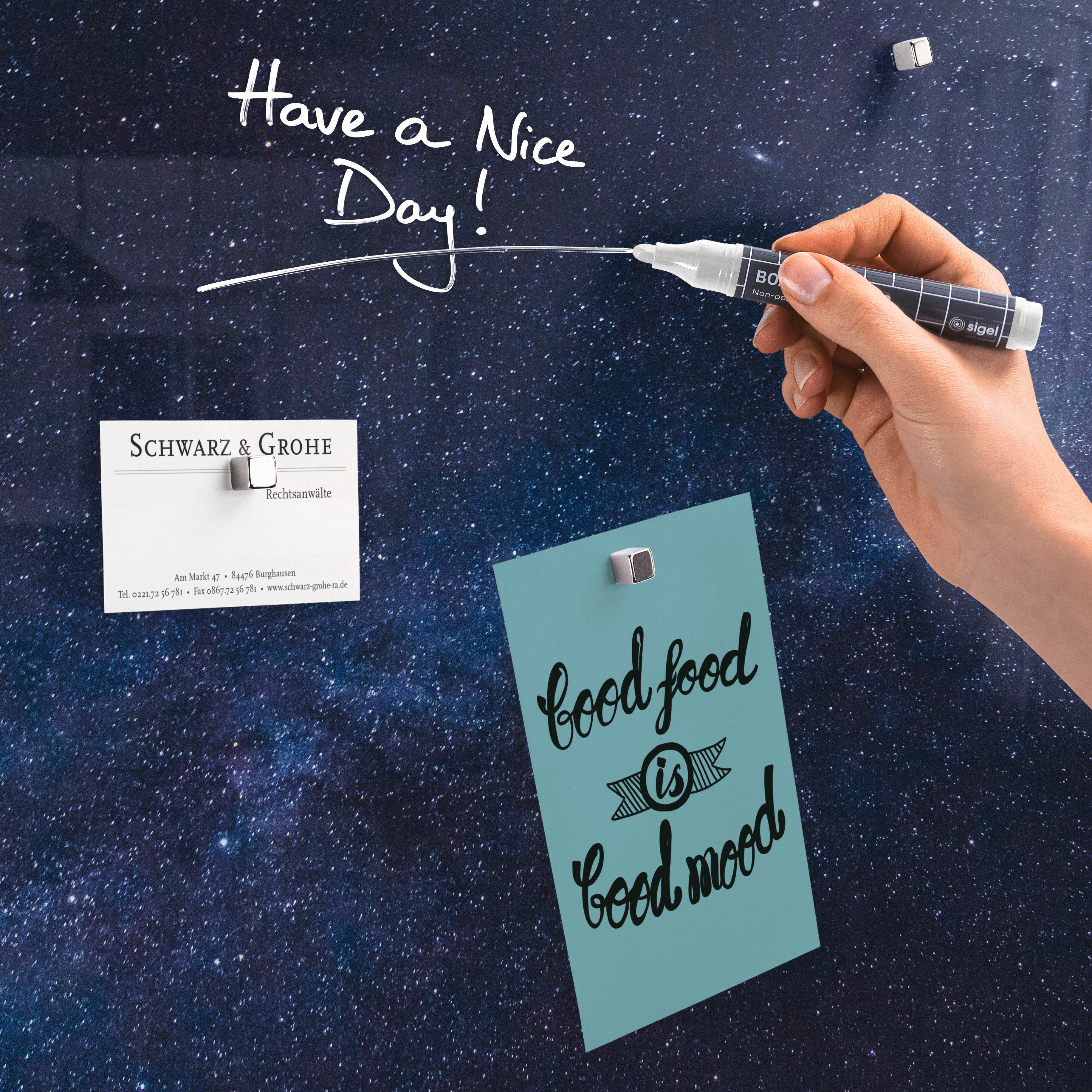 Hand, die einen Stift hält und 'Have a Nice Day!' auf einen Sternenhintergrund schreibt. Notizen mit Magneten befestigt, mit 'good food is good mood'.