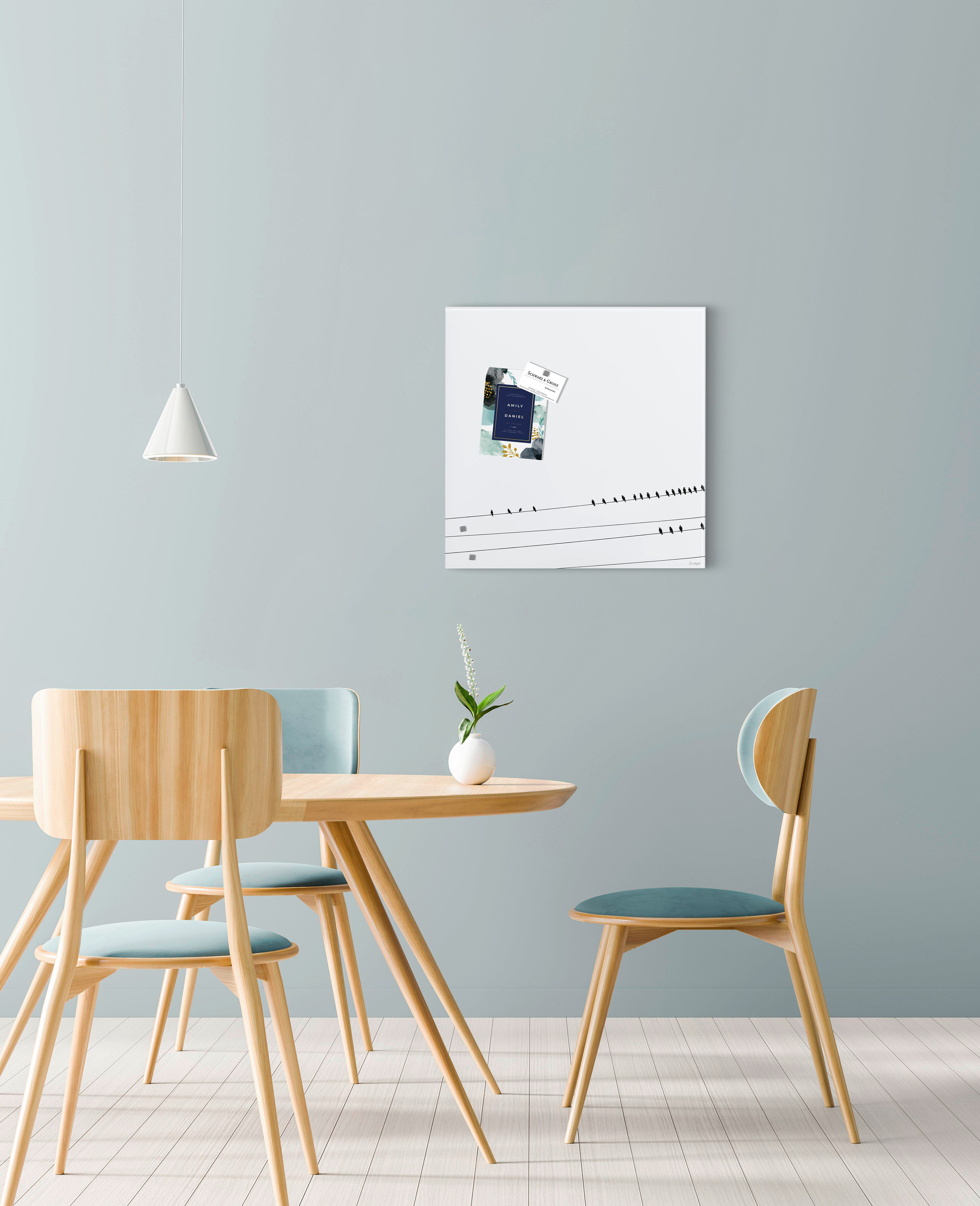 Esszimmer mit Tisch und Stühlen. An der Wand hängt ein Bild mit Vögeln auf einem Draht. Über dem Tisch hängt eine Lampe.