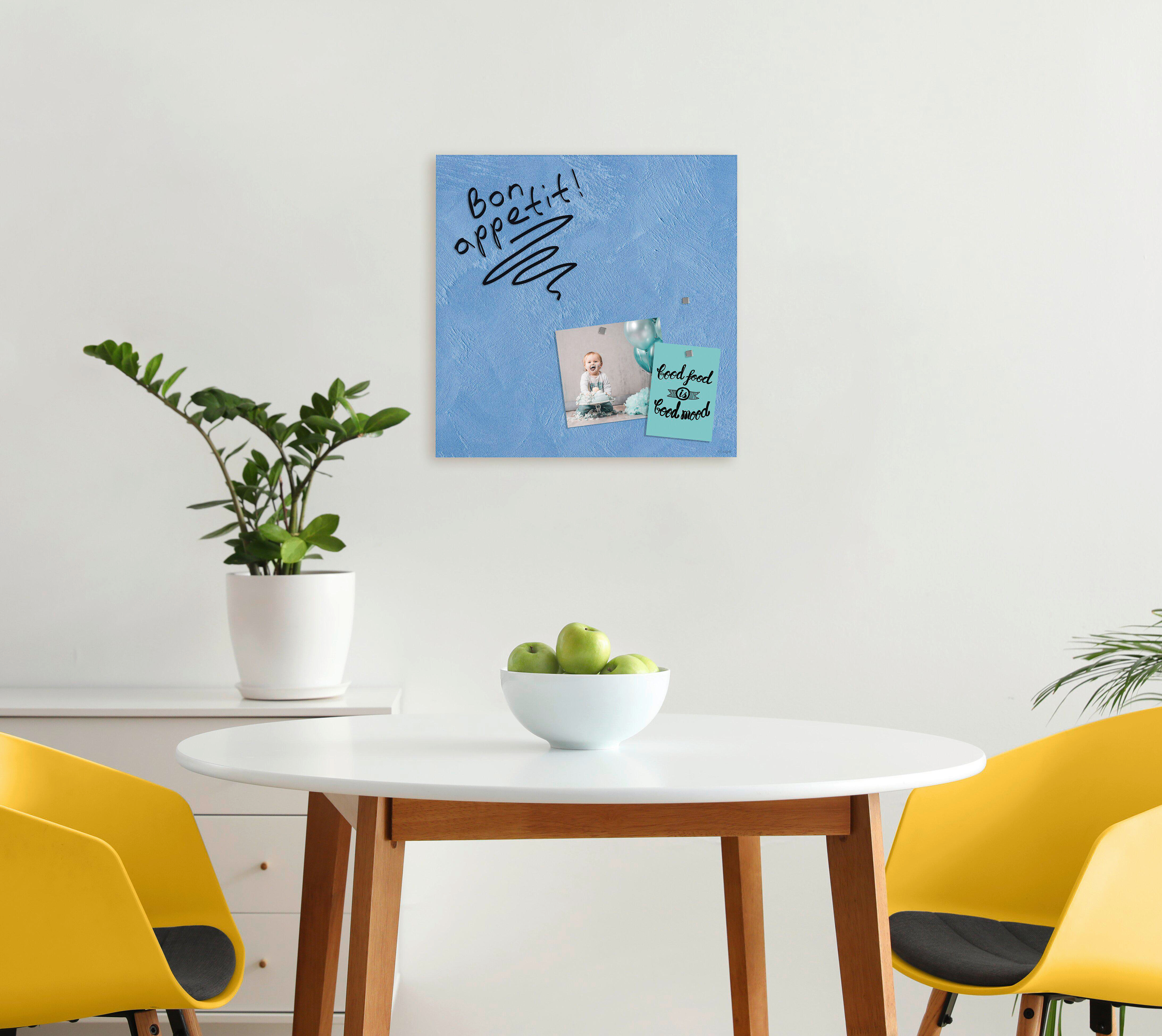 Ein Raum mit Tisch, Stühlen, einer Pflanze und einer Tafel mit Bild und Text.