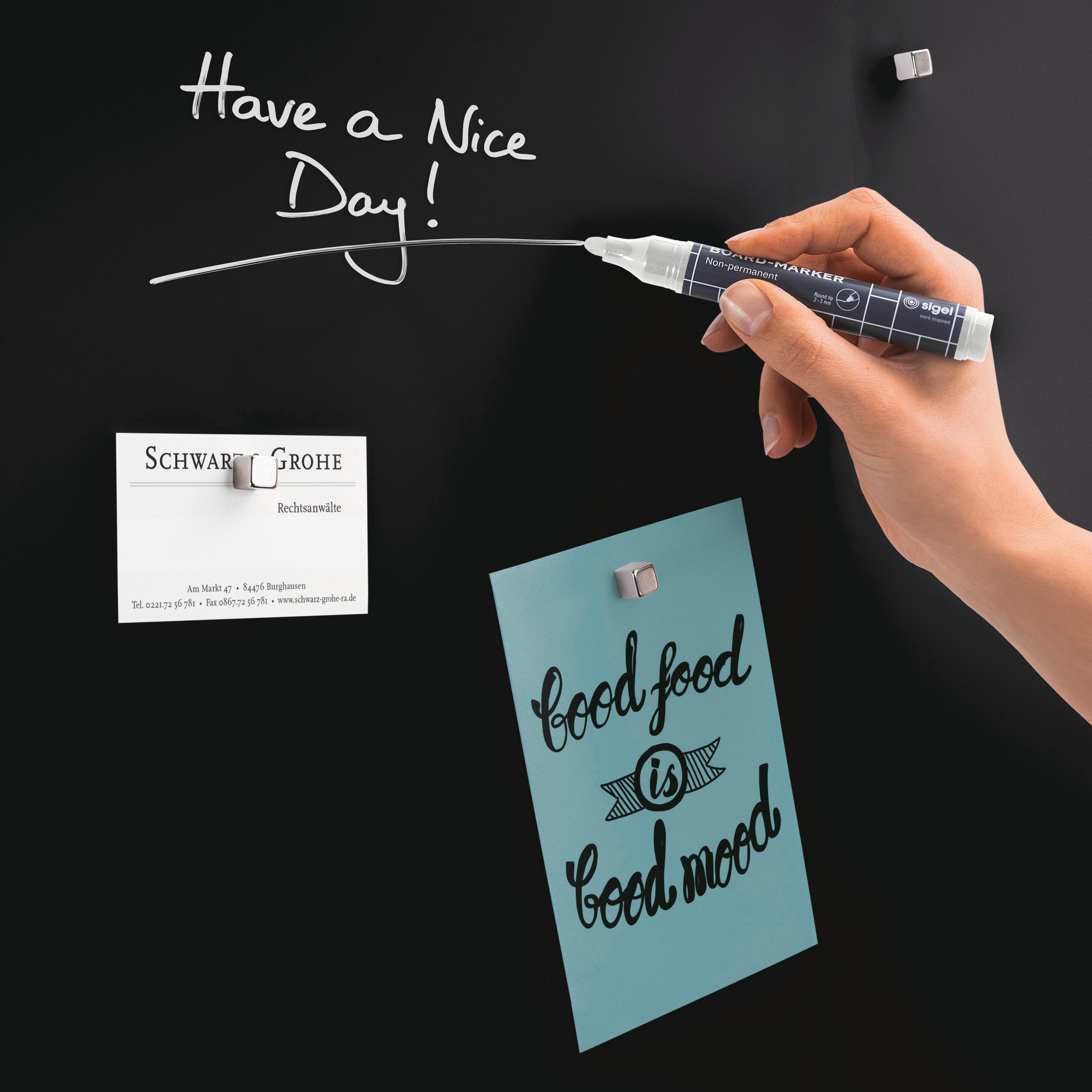 Eine Hand, die einen Marker auf einer schwarzen Oberfläche hält, mit Text: Have a Nice Day und anderen Notizen.