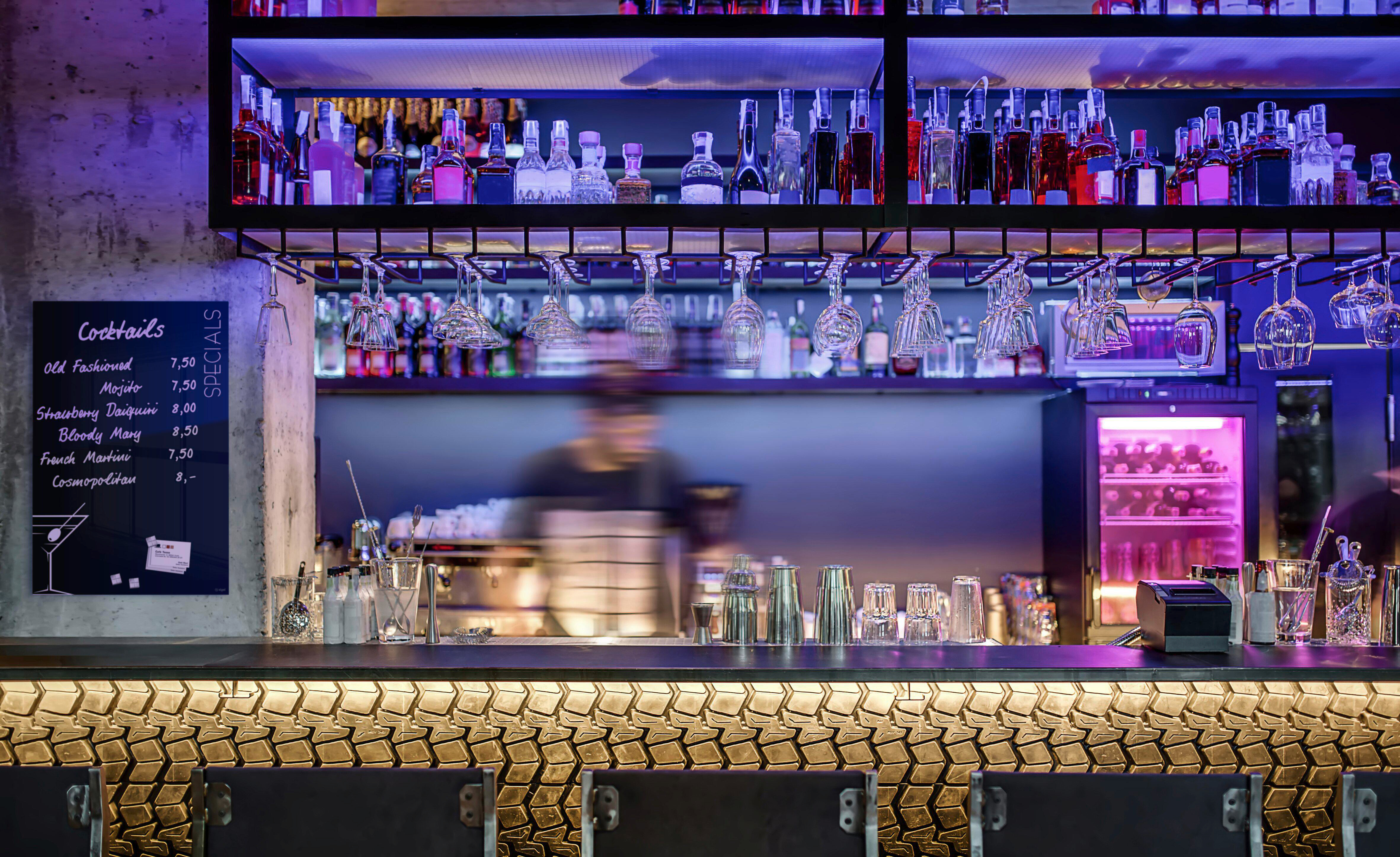 Eine Bar mit Flaschen, Gläsern und einer Cocktailkarte. Die Bar hat eine strukturierte Front und hängende Gläser.
