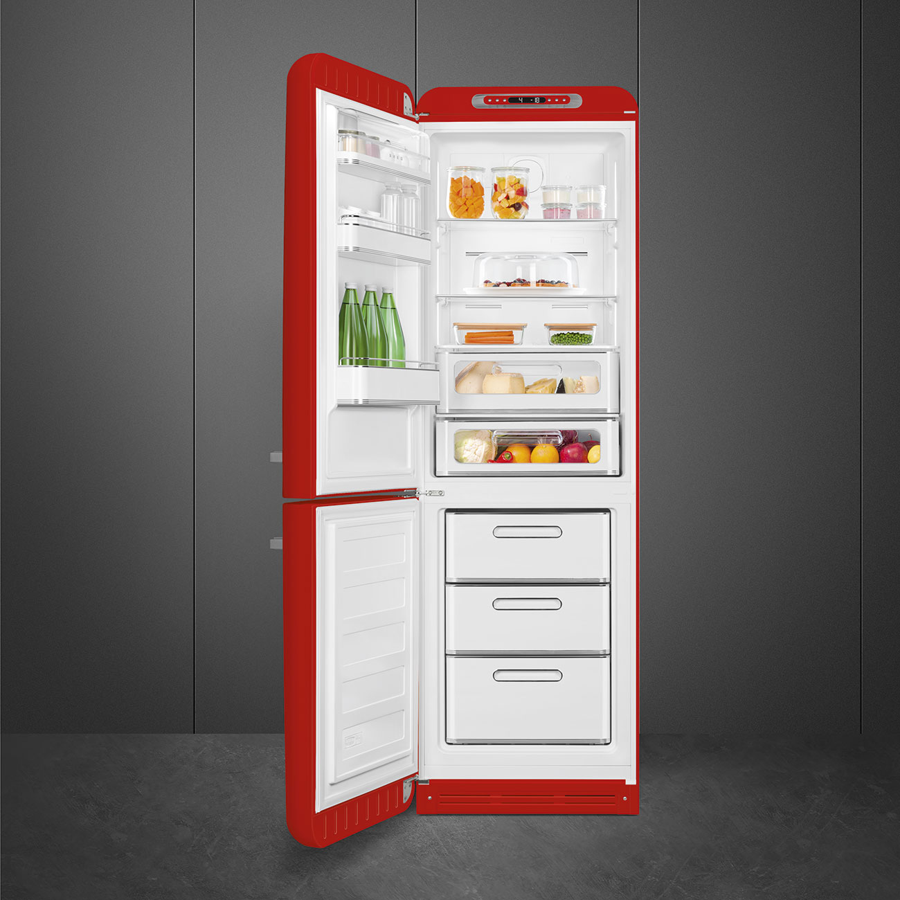 Offener roter Kühlschrank mit Lebensmitteln gefüllt: Gläser, Gemüse, Obst, Käse und Flaschen. Graue Wand und Boden im Hintergrund.