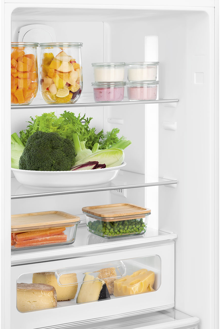 In einem Kühlschrank: Früchte, Gemüse, Joghurt und Käse sind gelagert. Karotten und Erbsen in Glasbehältern.