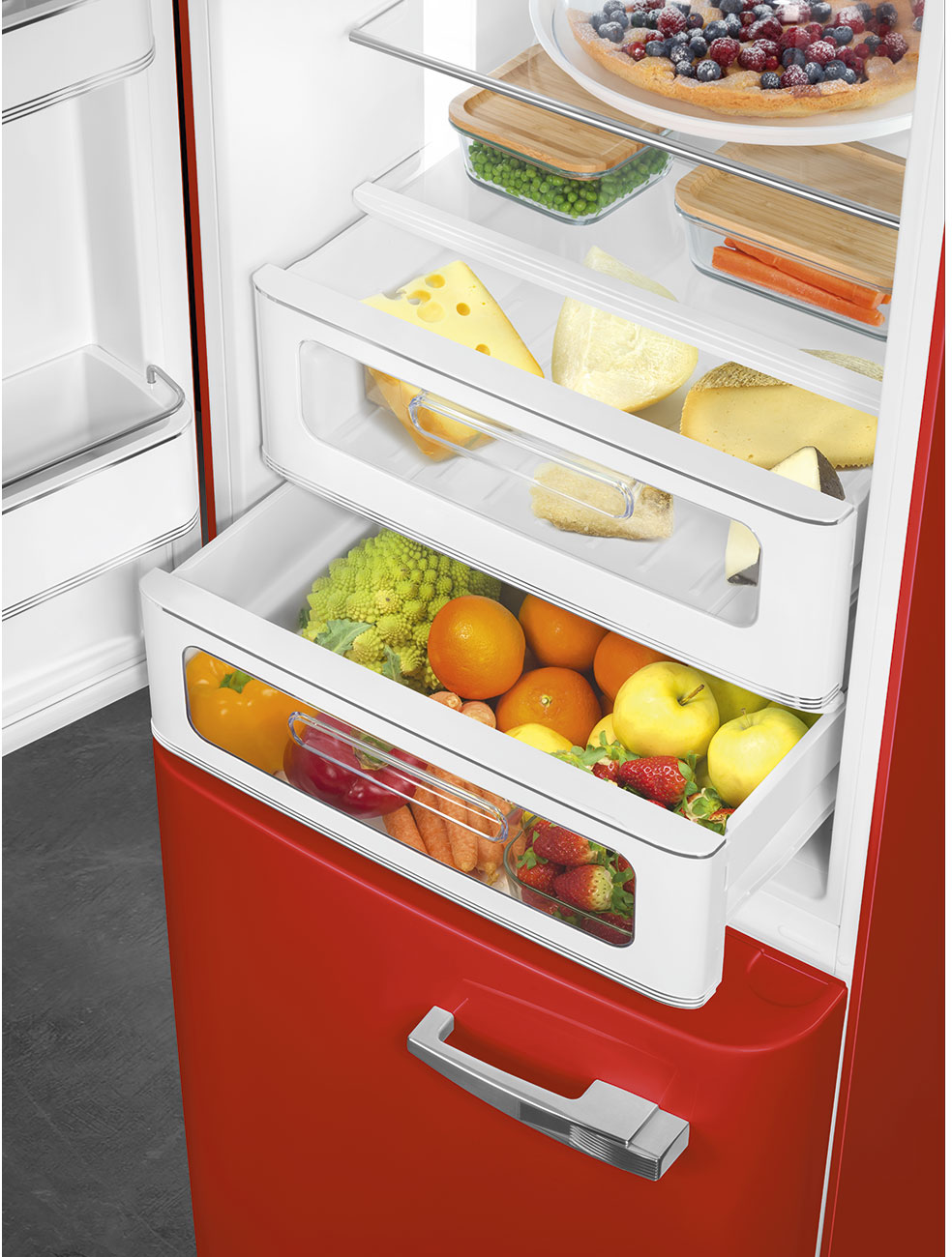 Roter Kühlschrank geöffnet, gefüllt mit Essen: Käse, Obst, Gemüse und einem Kuchen. Regale und Schubladen sind sichtbar.