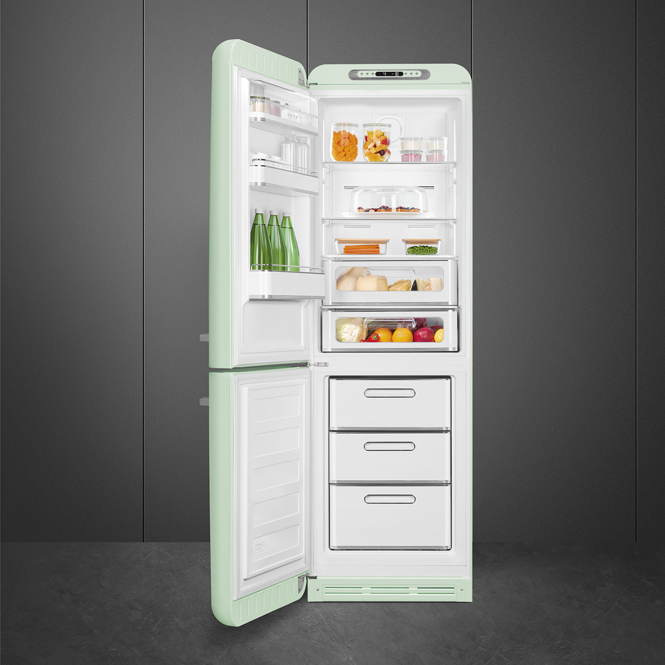 Offener mintgrüner Kühlschrank mit Lebensmitteln gefüllt. Gläser, Produkte und Schubladen sichtbar. Dunkelgrauer Hintergrund und grauer Boden.