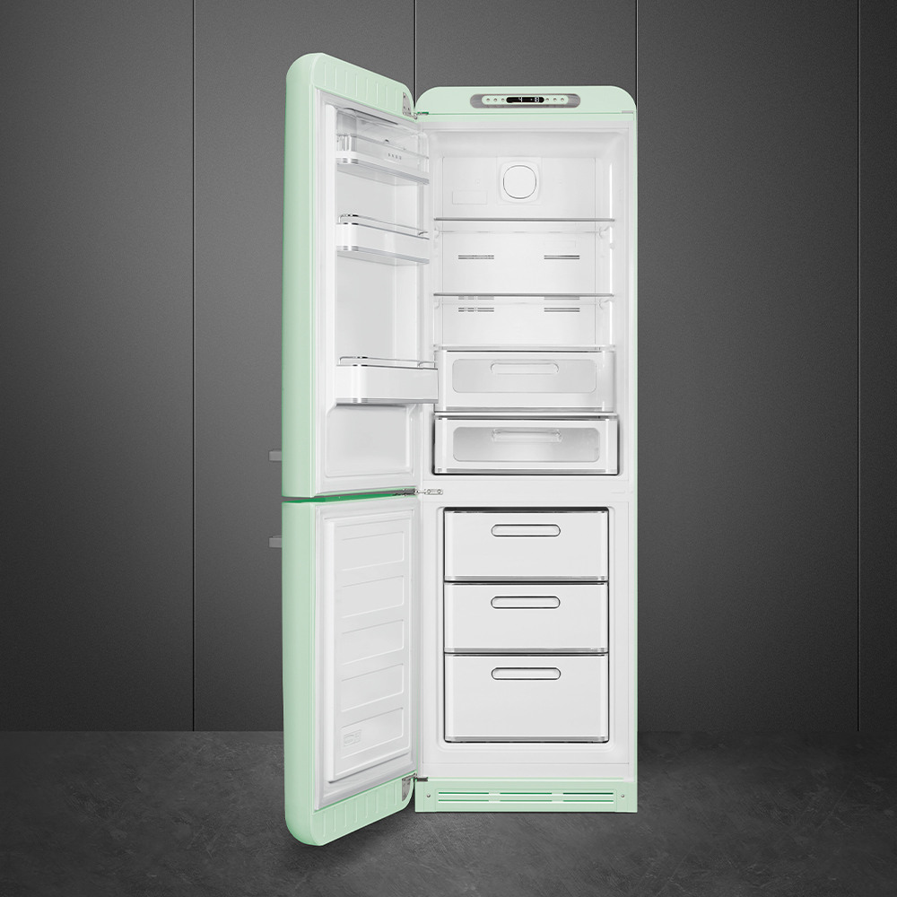 Offener mintgrüner Retro-Kühlschrank. Innenraum mit Regalen, Schubladen und Fächern. Grauer Hintergrund und Betonboden.