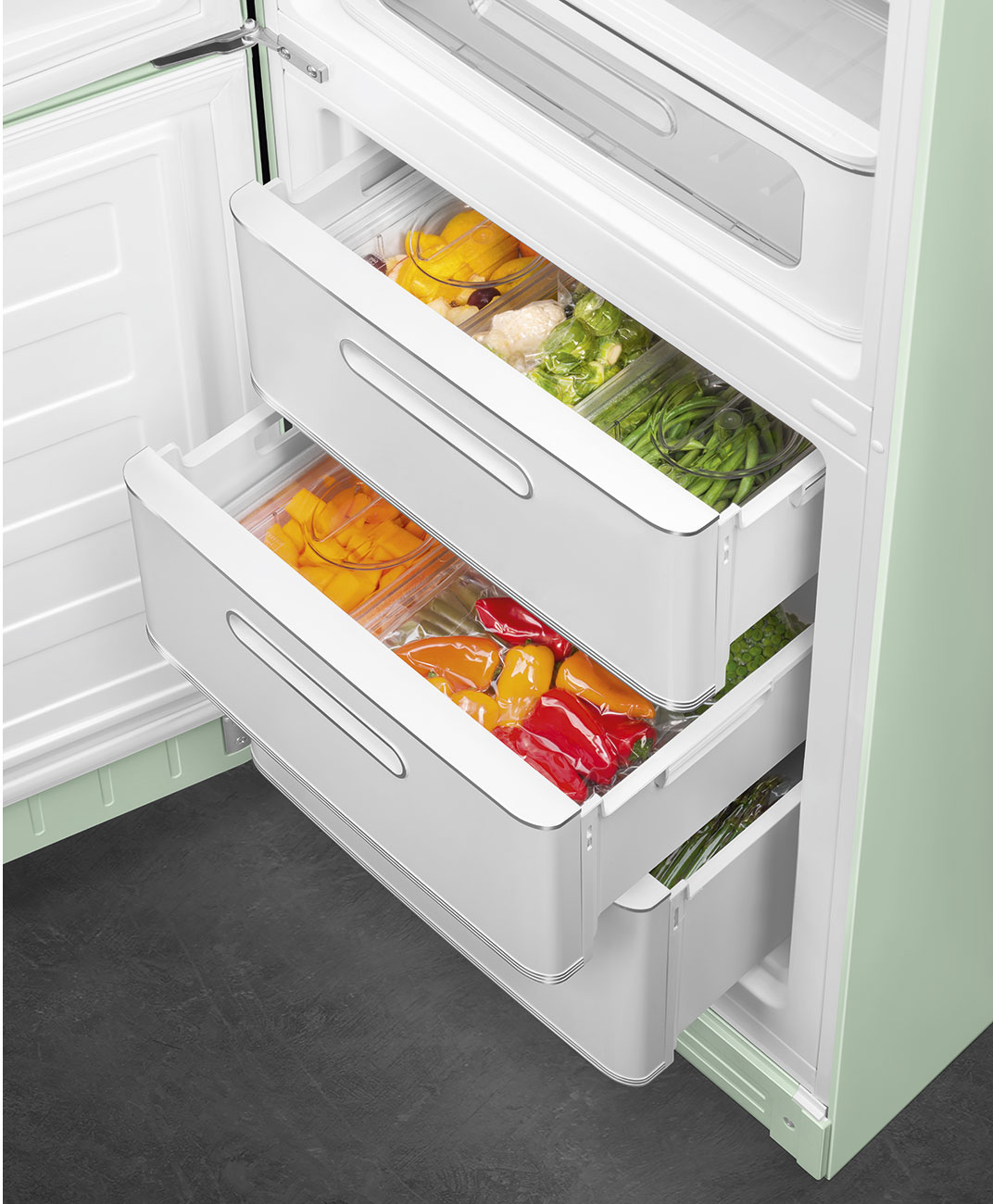 Offener Kühlschrank mit Schubladen voller bunter Paprika, grüner Bohnen und anderem Gemüse. Weiße Schubladen, grüner Kühlschrank.