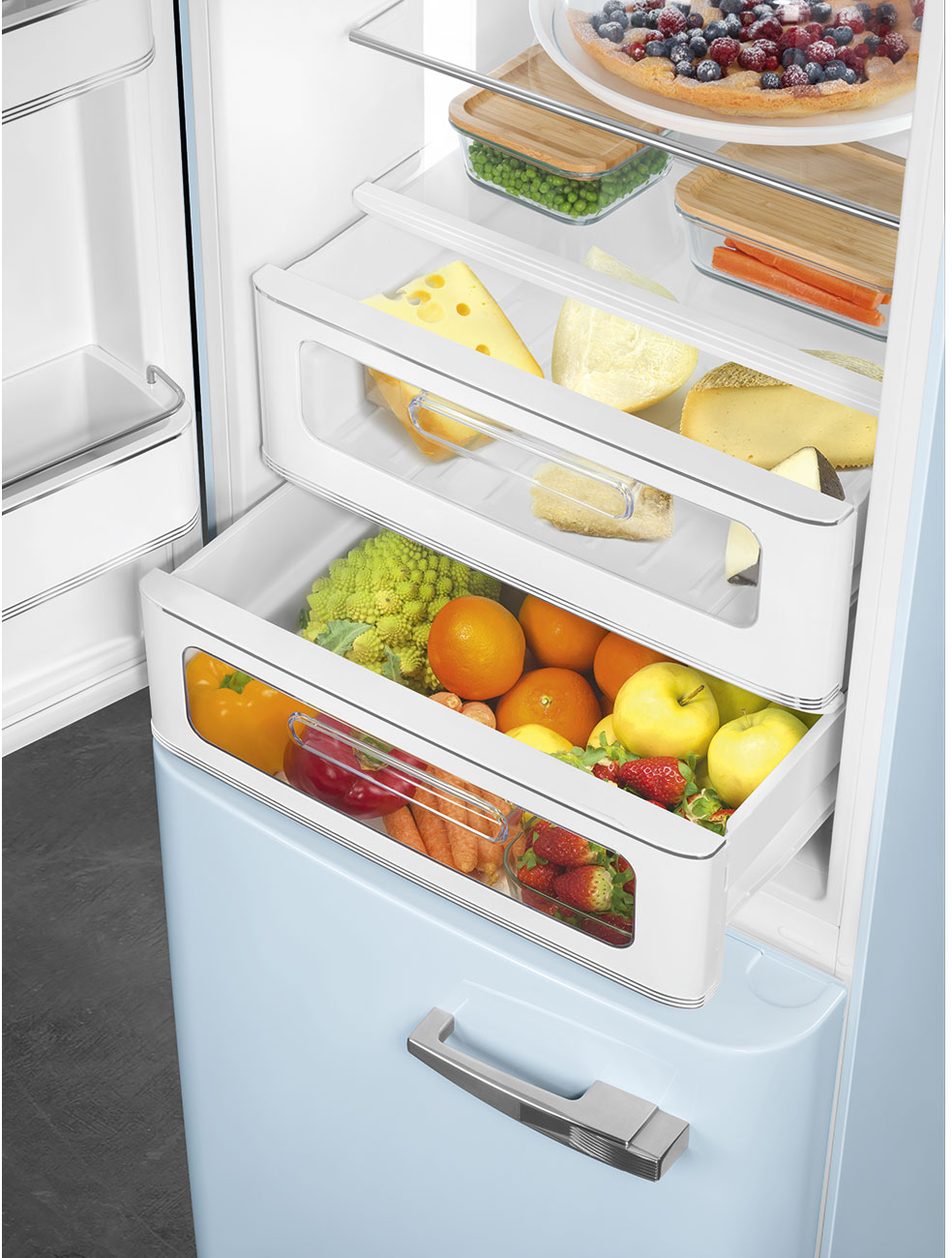 Offener Kühlschrank mit Früchten, Käse und Gemüse. Enthält Orangen, Äpfel, Erdbeeren und Karotten.