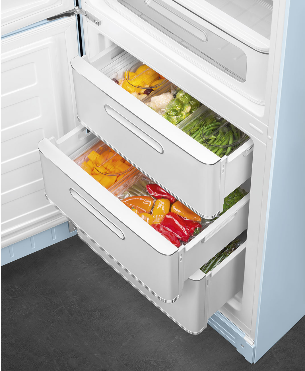 Offener Kühlschrank mit Schubladen voller bunter Paprika und Gemüse. Blaues und weißes Innere. Dunkelgrauer Boden.
