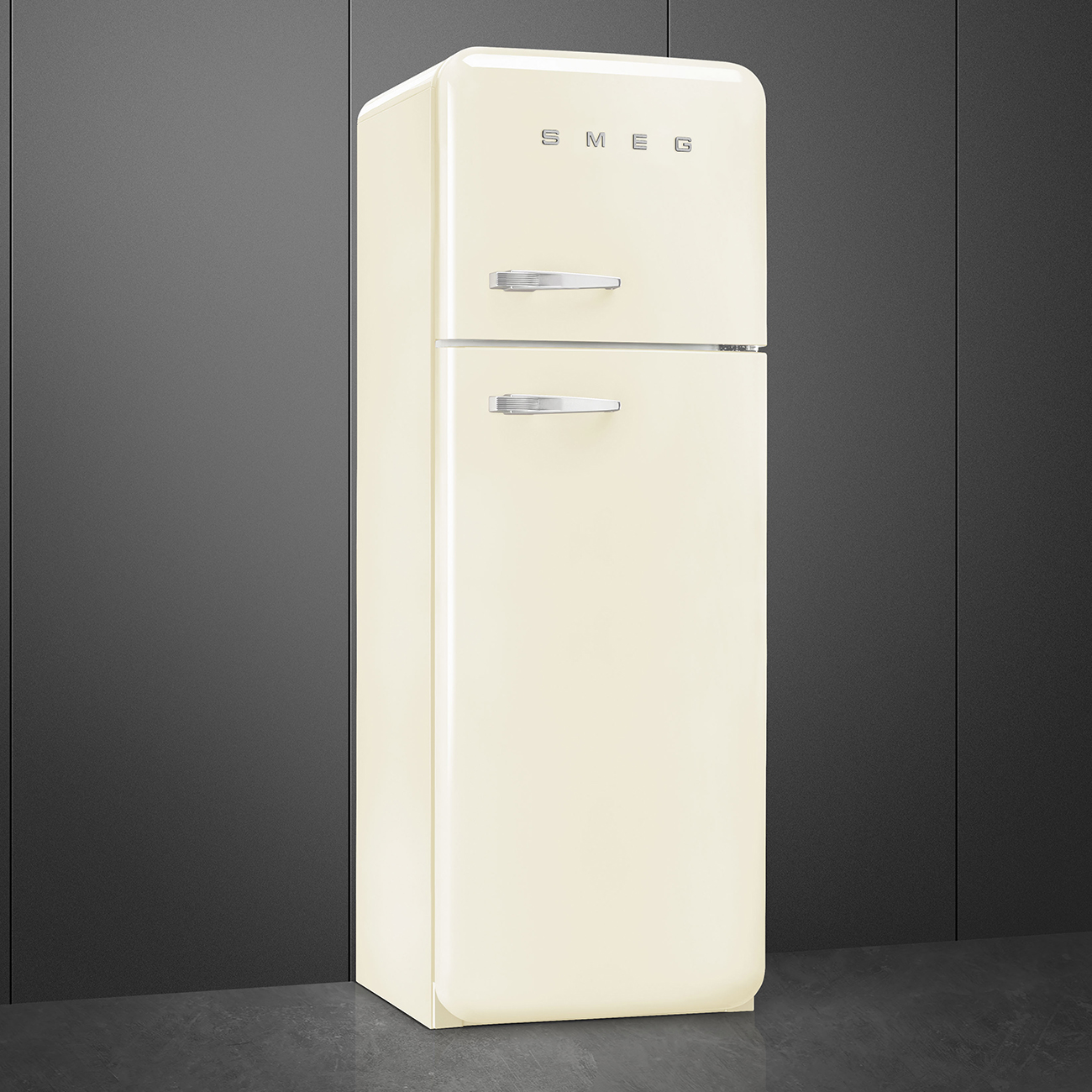 Ein cremefarbener SMEG-Kühlschrank steht vor einer dunkelgrauen Wand. Er hat zwei Türen mit silbernen Griffen und das SMEG-Logo.