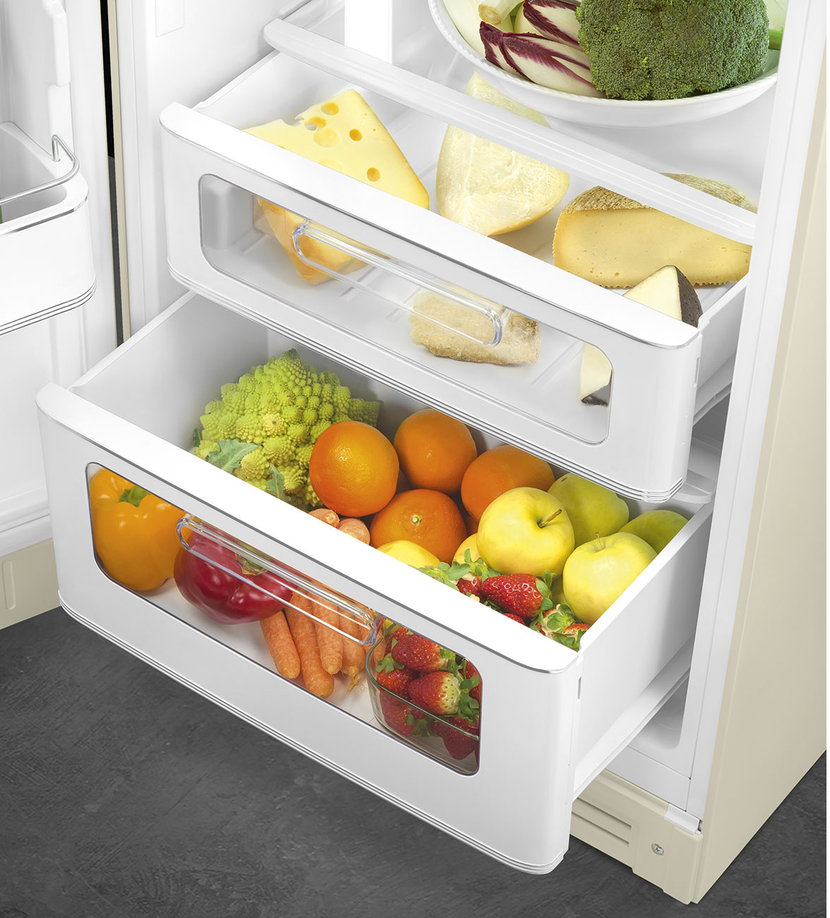 In einem Kühlschrank befinden sich Schubladen mit Obst, Gemüse und Käse. Brokkoli, Erdbeeren, Orangen und Äpfel sind vorhanden.