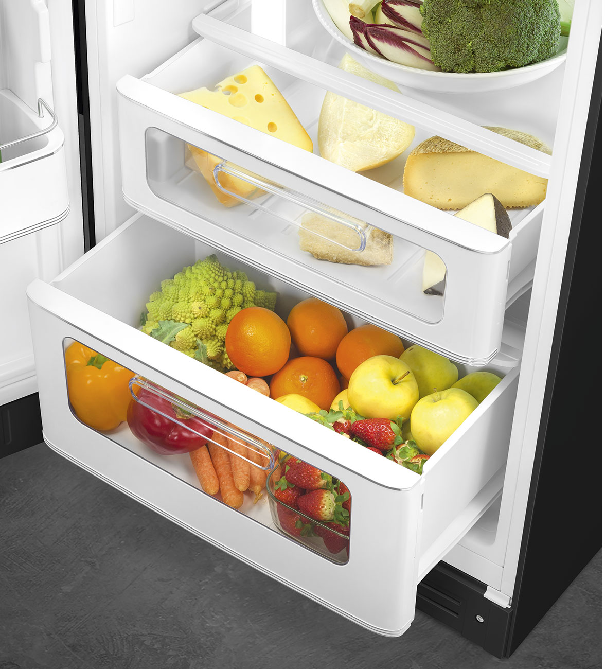 Im Kühlschrank: Käse, Orangen, Äpfel und Gemüse. Erdbeeren in einem Glasbehälter. Weiße Schubladen.