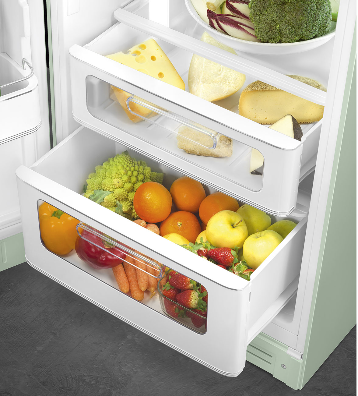Im Kühlschrank sind Schubladen mit Gemüse und Käse gefüllt. Orangen, Äpfel und Erdbeeren sind in den Schubladen zu sehen.