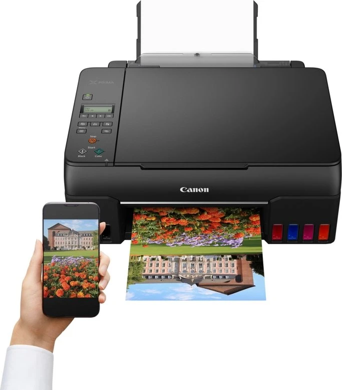 Ein schwarzer Canon-Drucker druckt ein Foto. Eine Hand hält ein Telefon, das dasselbe Bild zeigt. Das gedruckte Bild spiegelt das Gebäude wider.