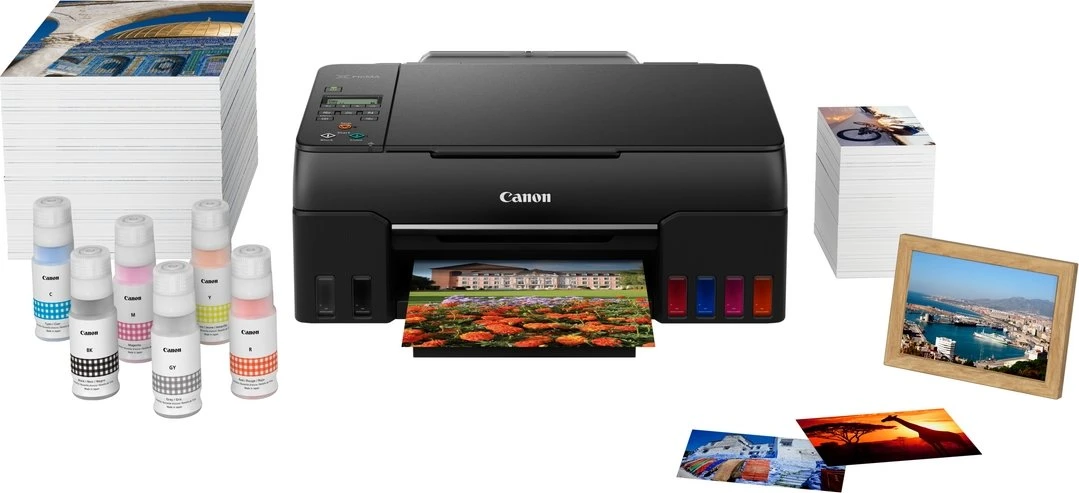 Ein schwarzer Canon-Drucker mit Fotos, Tintenflaschen und Papierstapeln, einer mit einem Kuppelbild und einem gerahmten Hafenblick.