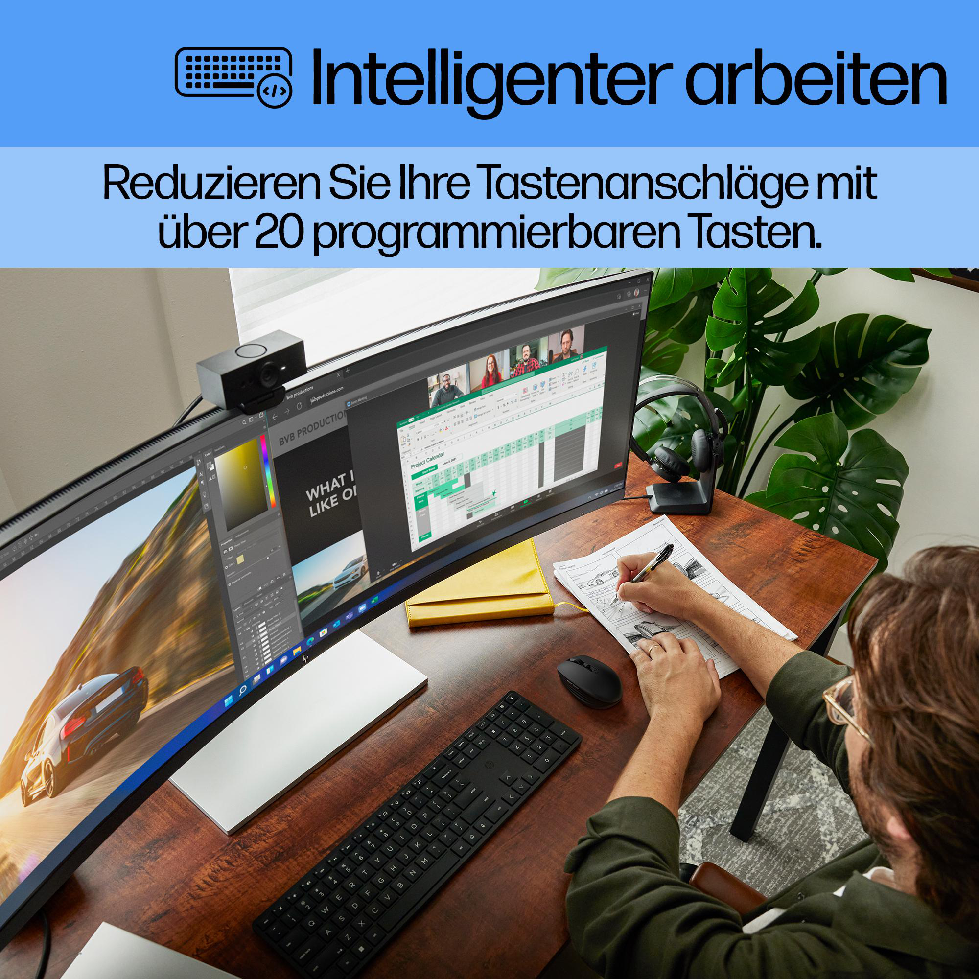 Eine Person arbeitet an einem Schreibtisch mit Computer und Tastatur. Auf dem Bildschirm ist ein Videoanruf und eine Zeichnung auf Papier zu sehen.