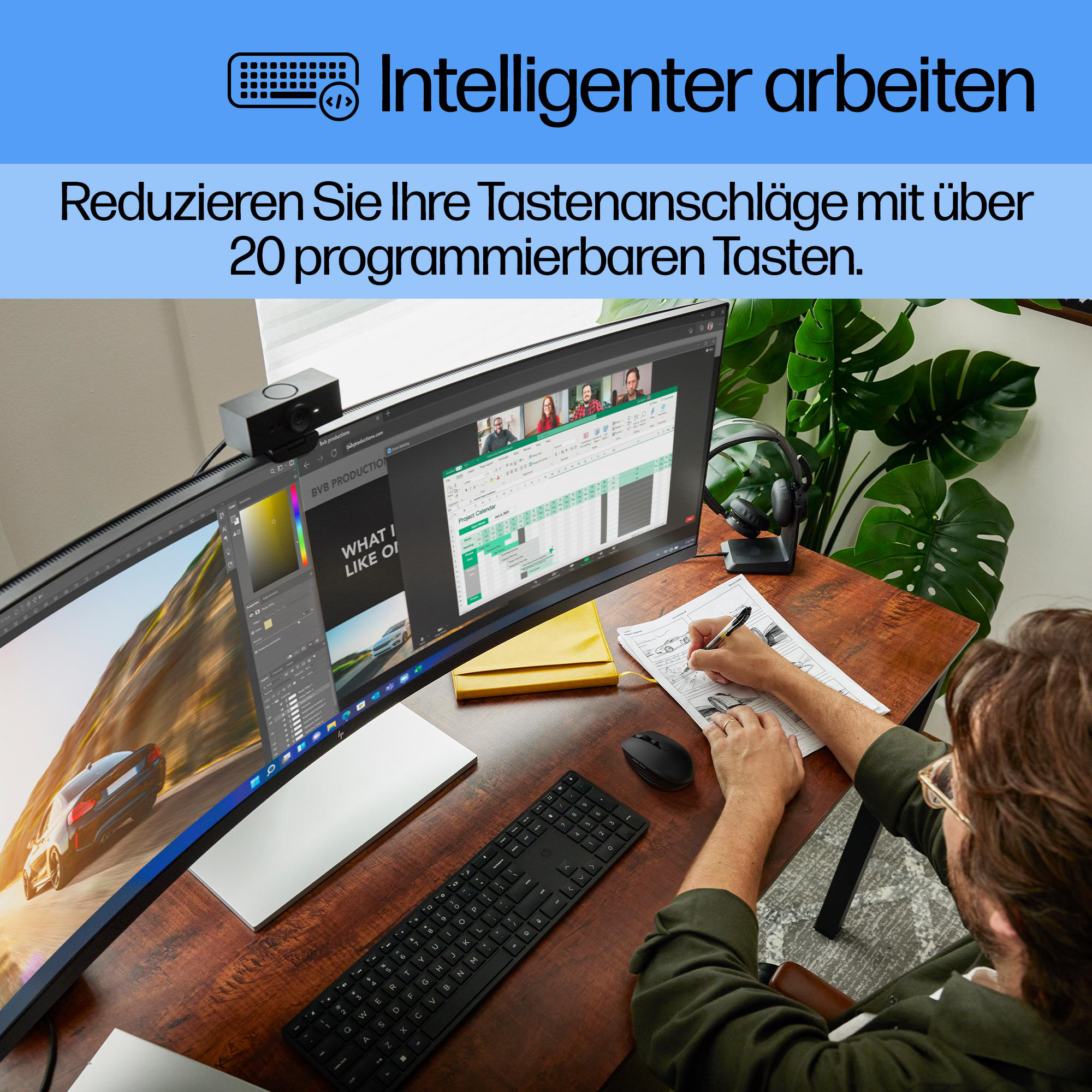 Eine Person arbeitet an einem Schreibtisch mit Tastatur, Maus und Monitor und schreibt auf Papier. Auf dem Bildschirm ist ein Videoanruf zu sehen.