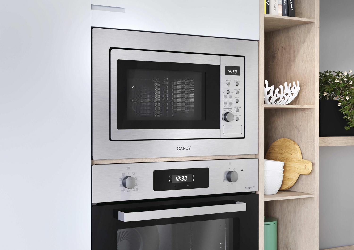 Microondas y horno de acero inoxidable integrados en un armario blanco. Estantes a la derecha con decoración y plantas.
