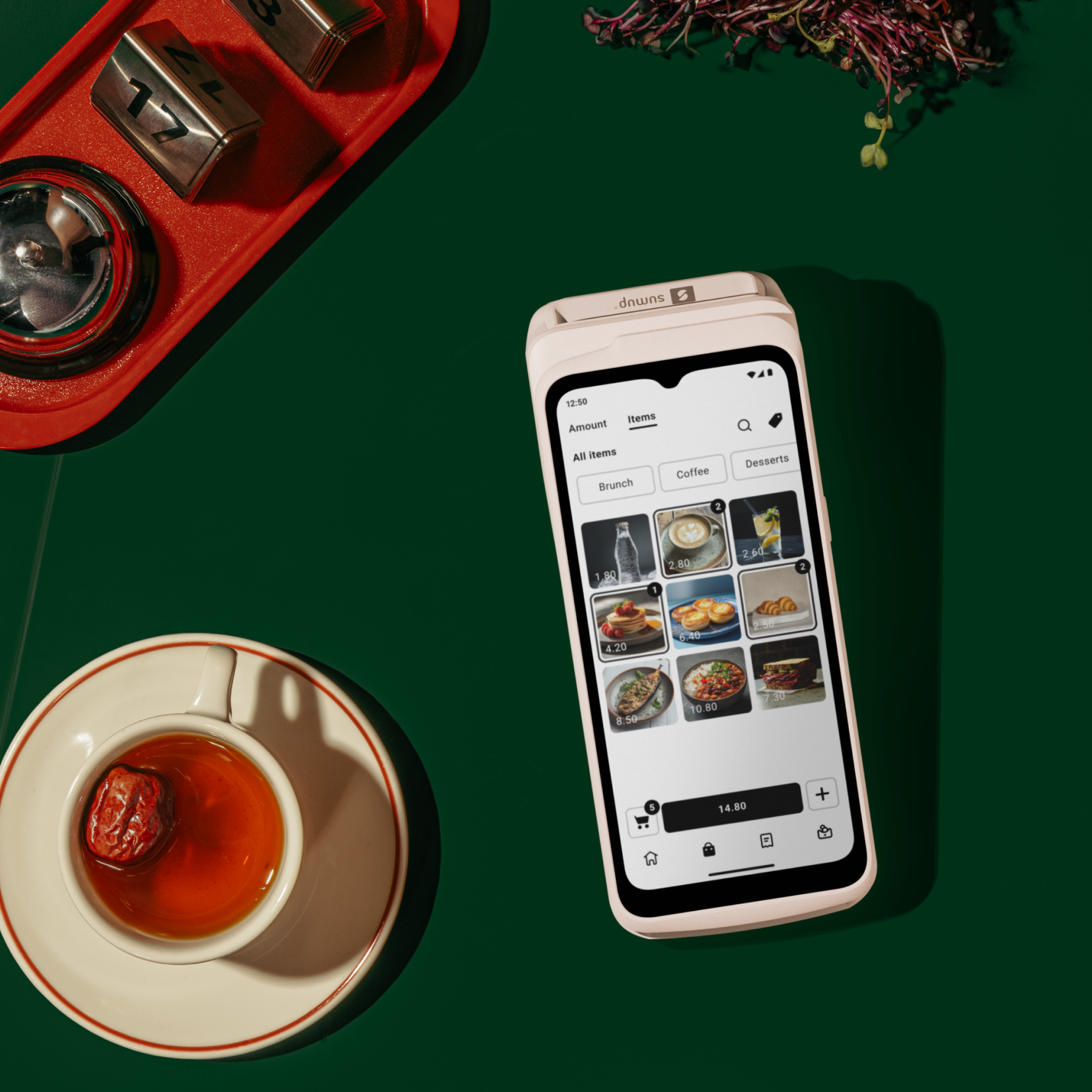 Una mesa con un teléfono que muestra un menú, té y un timbre. El fondo es verde oscuro.