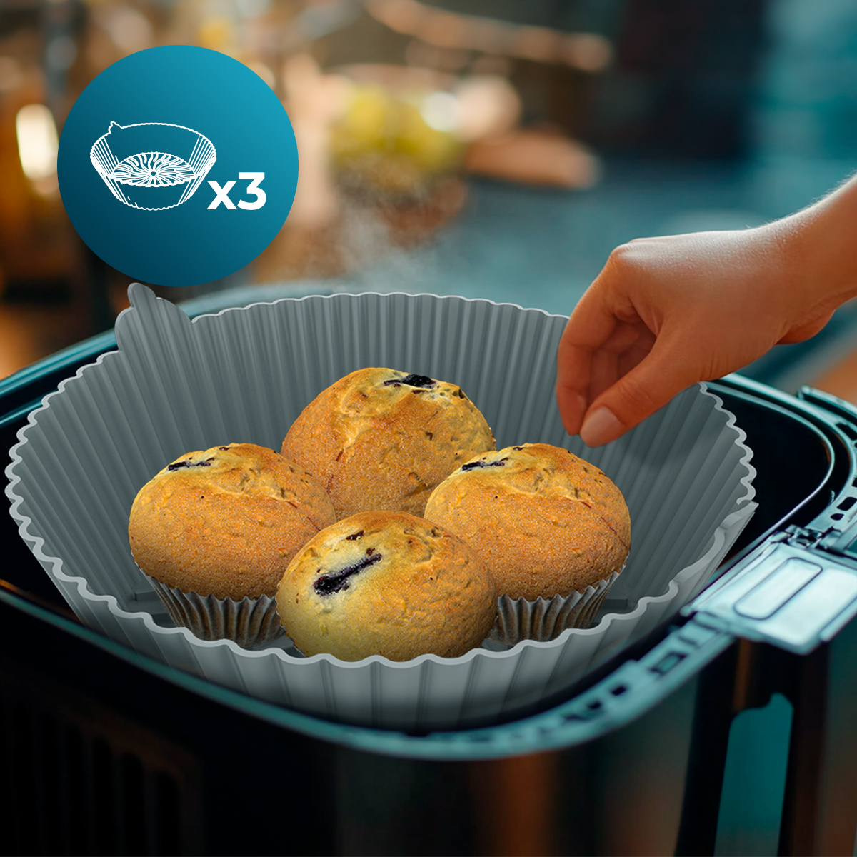 Cuatro muffins en una bandeja para hornear gris se colocan en una freidora de aire. Una mano alcanza la bandeja. Un círculo muestra 'x3'.