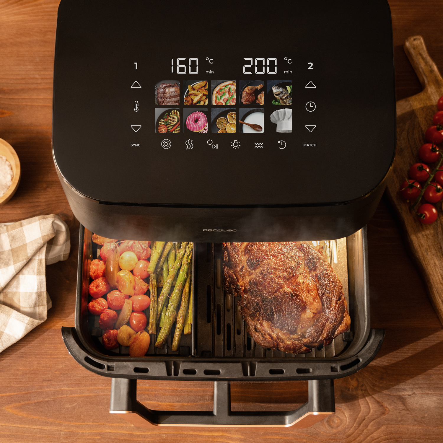 Una freidora de aire abierta con comida dentro, un bistec, verduras y una pantalla digital. Se ven tomates y espárragos.