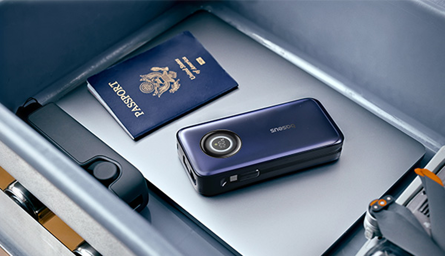 Dentro de un cajón, un pasaporte, un dispositivo azul oscuro y una unidad USB negra descansan sobre una superficie plateada.