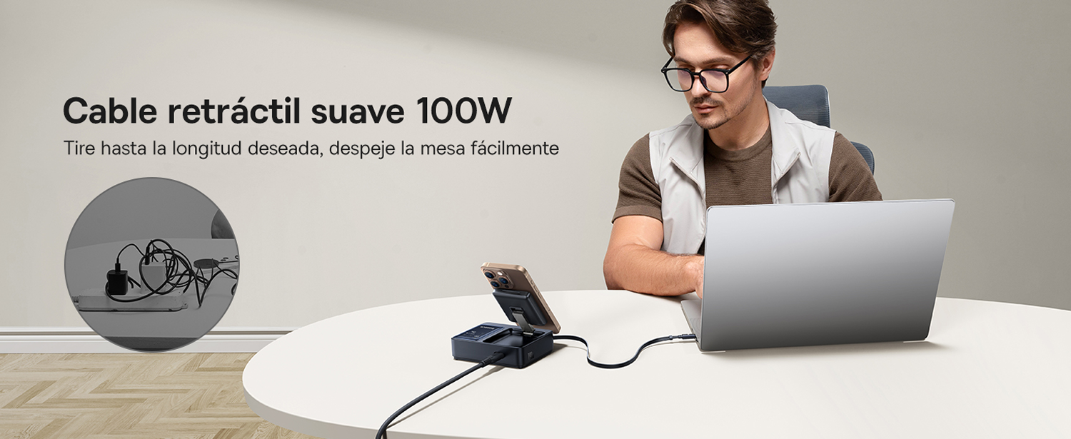 Hombre con gafas usando laptop. Teléfono en soporte. Cable retráctil sobre mesa blanca.