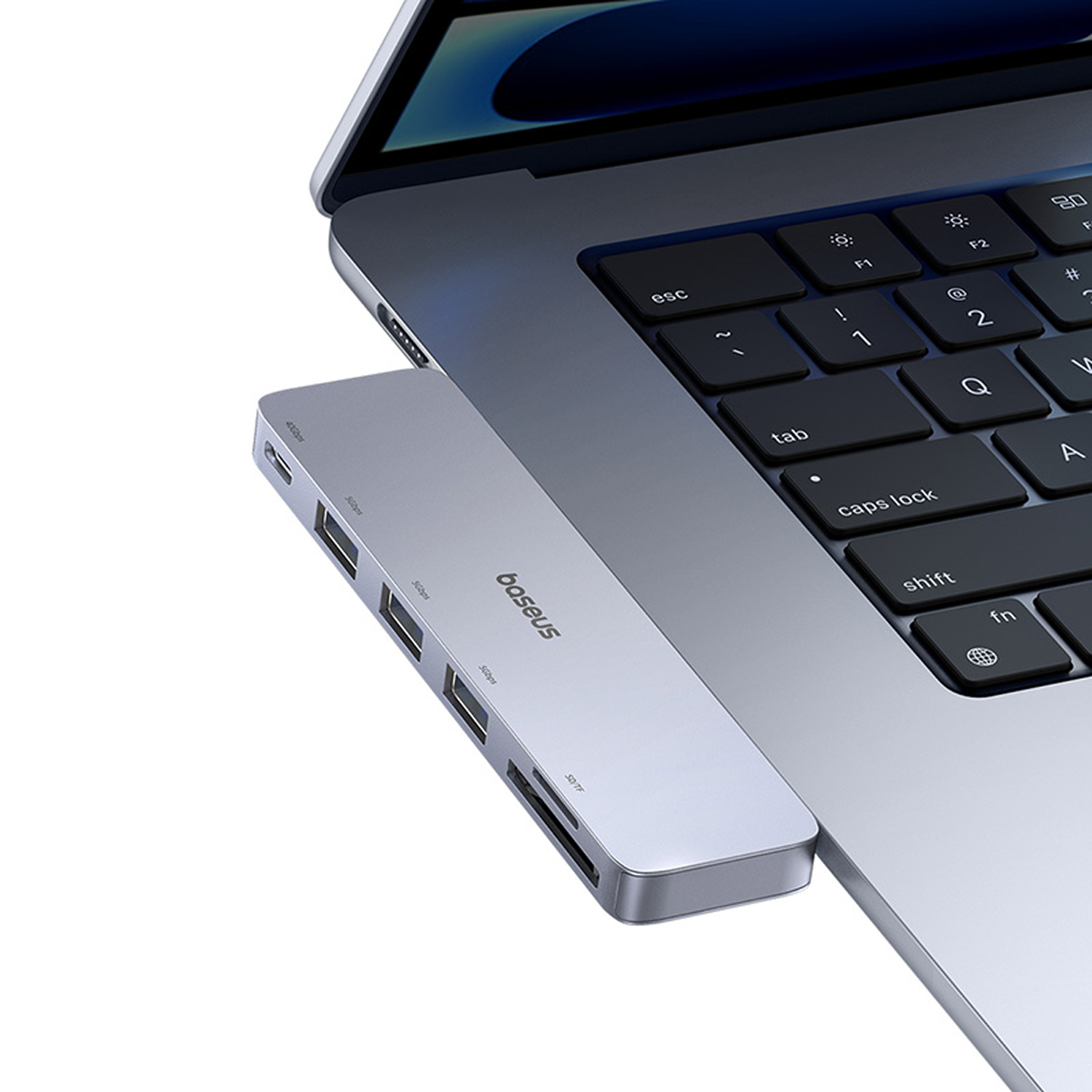 Un concentrador Baseus plateado está conectado a una computadora portátil. El concentrador tiene varios puertos. Se ve el teclado de la computadora portátil.