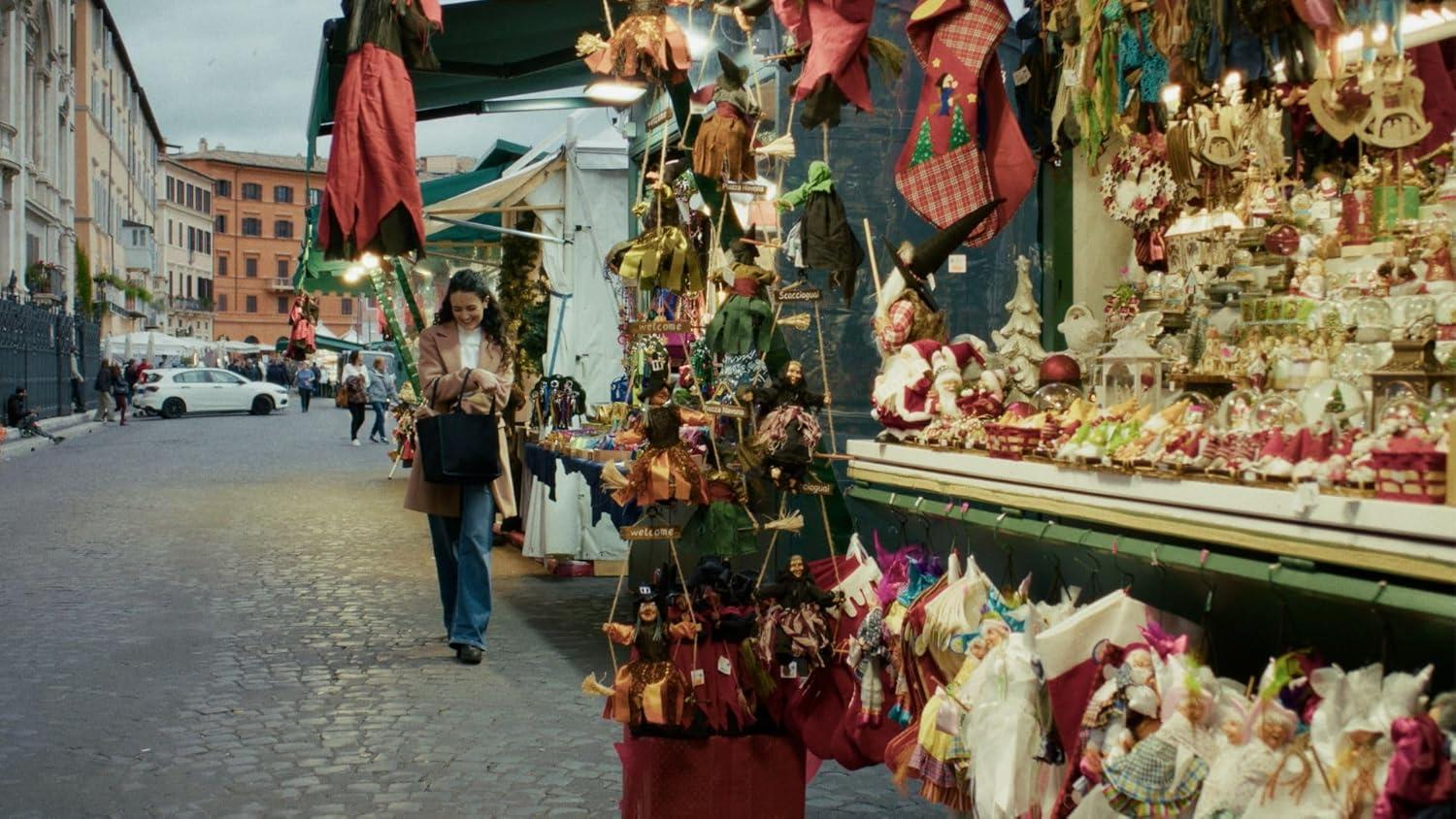 Eine Frau geht an Marktständen vorbei. Stände zeigen Kunsthandwerk und Weihnachtsdekorationen. Gebäude und ein Auto sind im Hintergrund.
