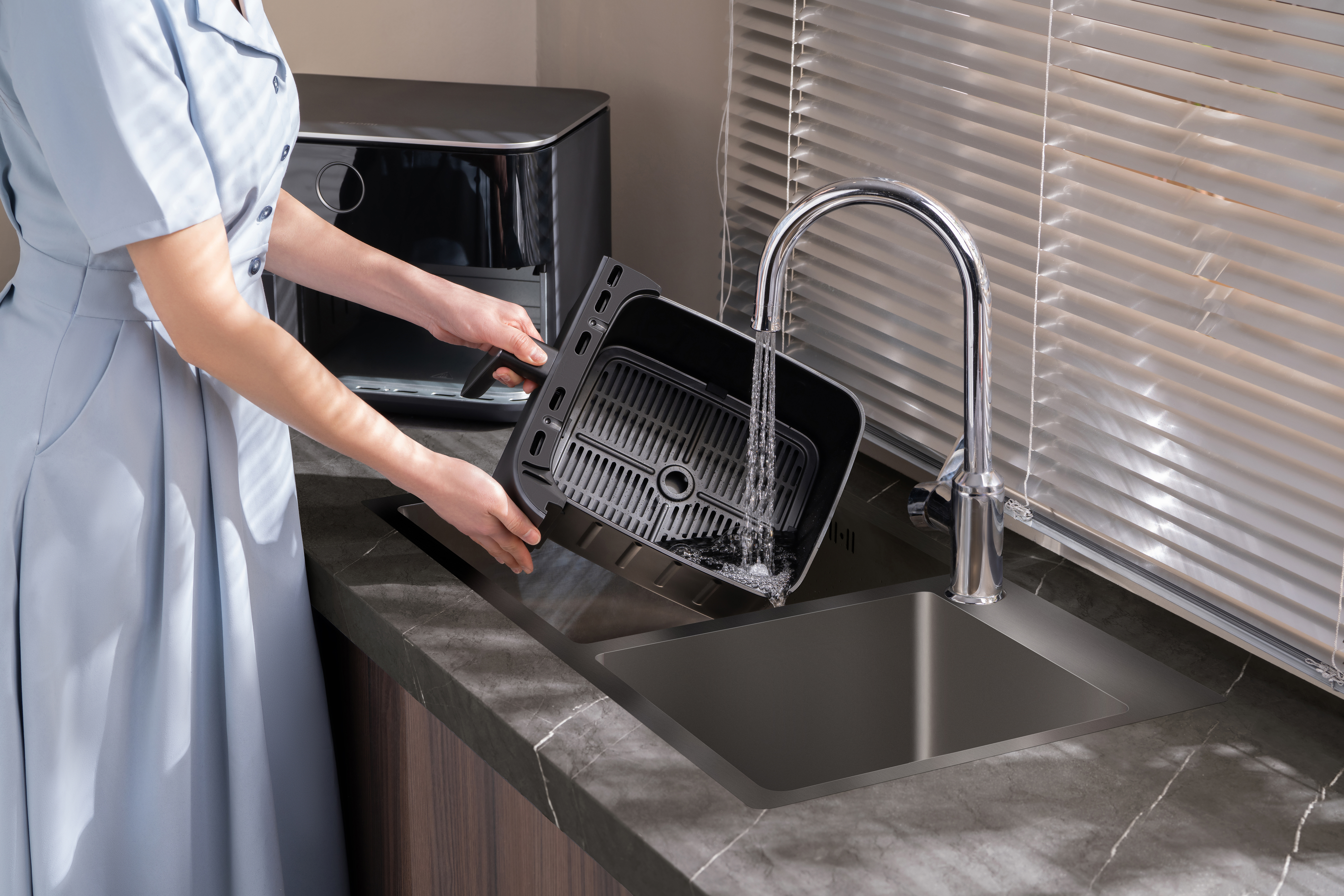 Eine Person wäscht einen schwarzen Luftfritteusenkorb in einem dunklen Waschbecken. Wasser fließt aus einem verchromten Wasserhahn.