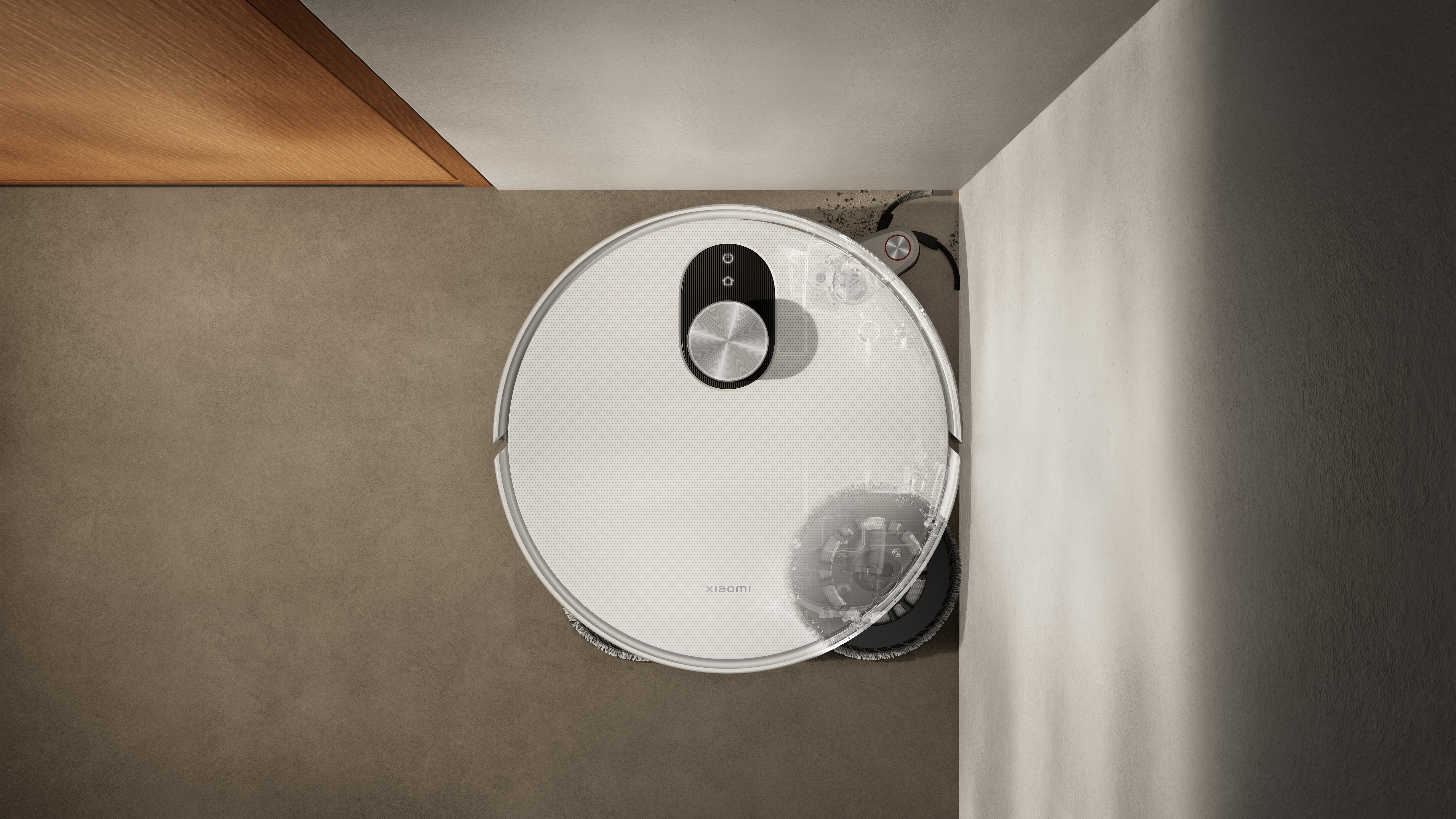 Draufsicht auf einen weißen Xiaomi-Roboterstaubsauger. Er reinigt eine Ecke neben einer Wand. Der Hintergrund zeigt Wände und eine Holzstruktur.