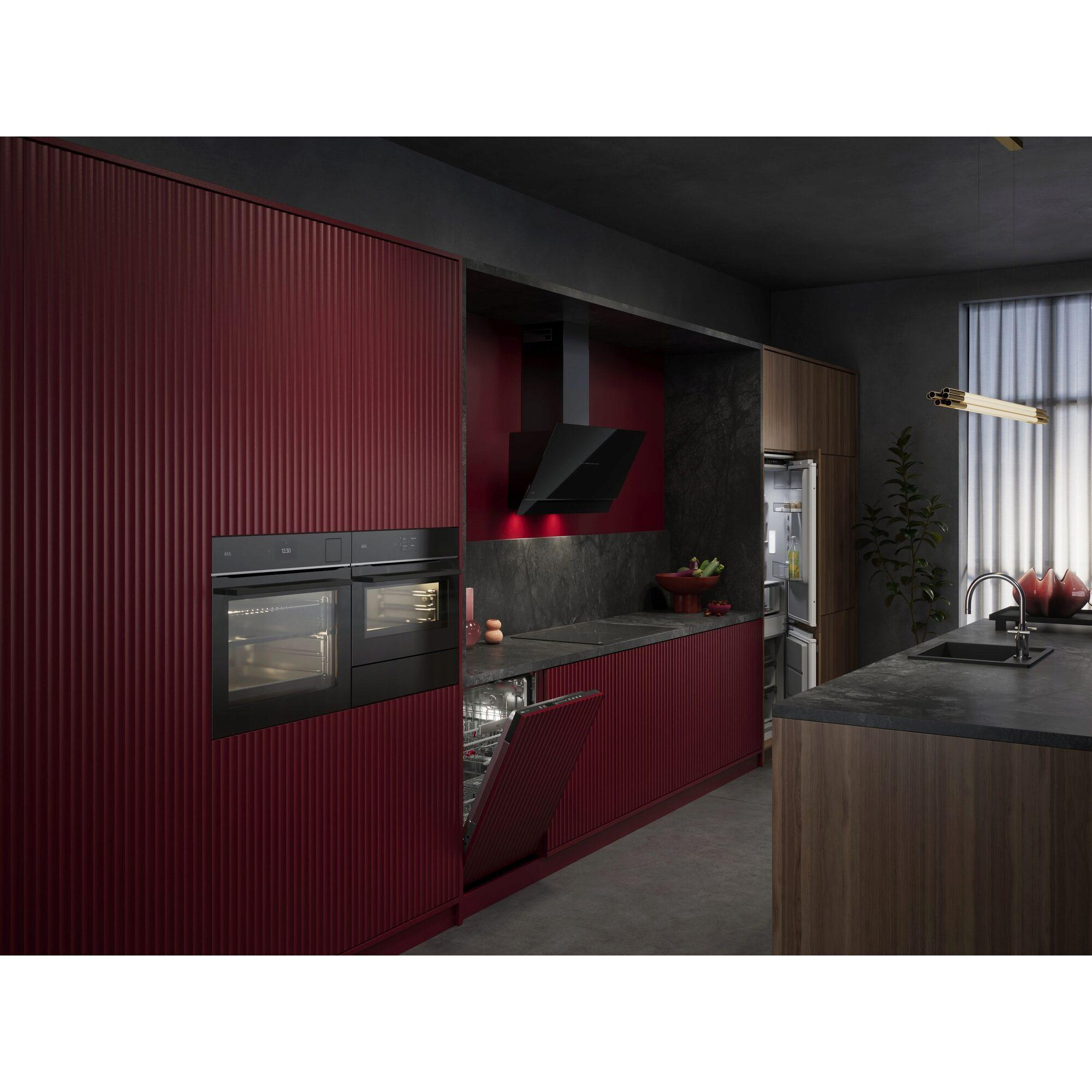 Moderne Küche mit roten Schränken, schwarzen Geräten und dunkler Arbeitsplatte. Geschirrspüler offen. Dekorative Beleuchtung und Pflanzen vorhanden.