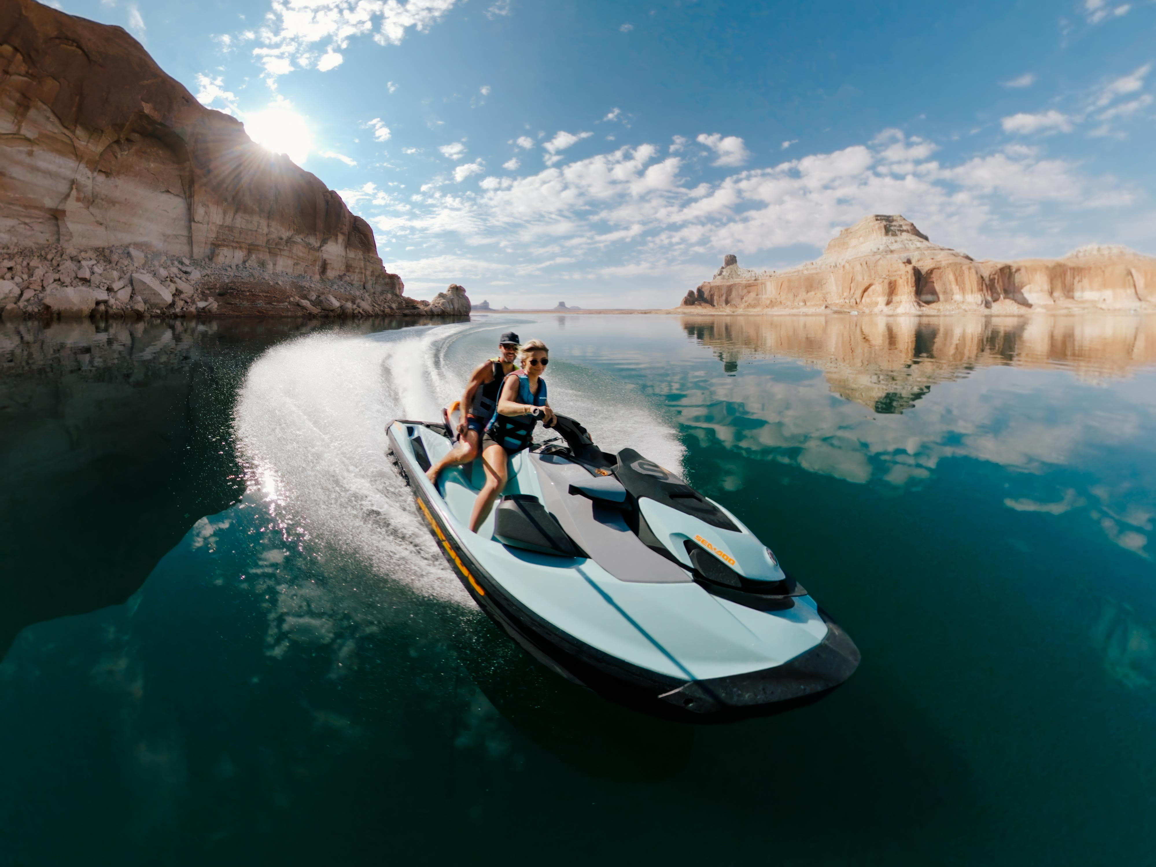 Ein Jetski mit zwei Personen auf einem See mit felsigen Klippen im Hintergrund unter blauem Himmel.