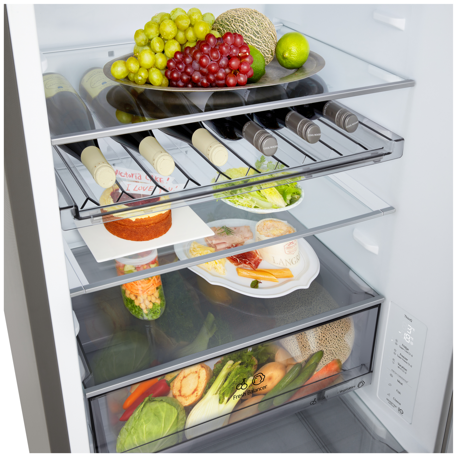 Open fridge with fruits, wine, cake, and vegetables. Various shelves display food items, with a digital temperature display on the side.