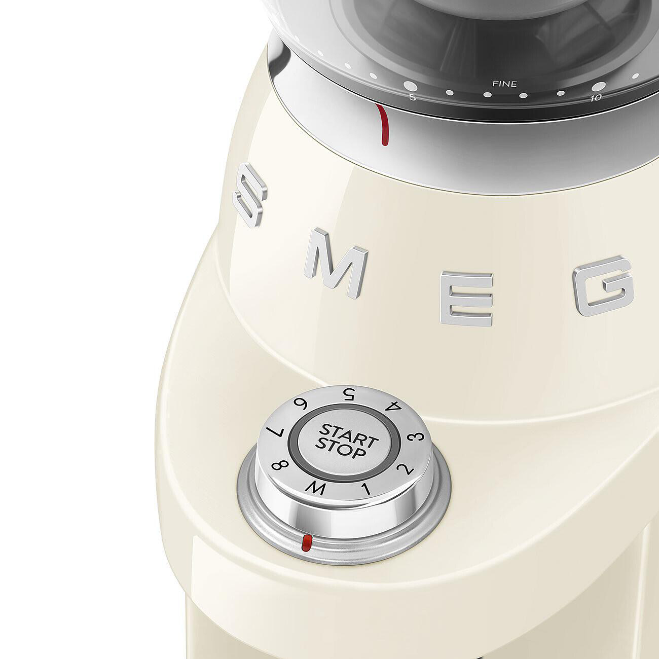 Cremefarbene SMEG-Kaffeemühle. Sie hat ein Start/Stopp-Rad, Zahlen und das Wort 'FEIN'. Die Mühle befindet sich auf weißem Hintergrund.
