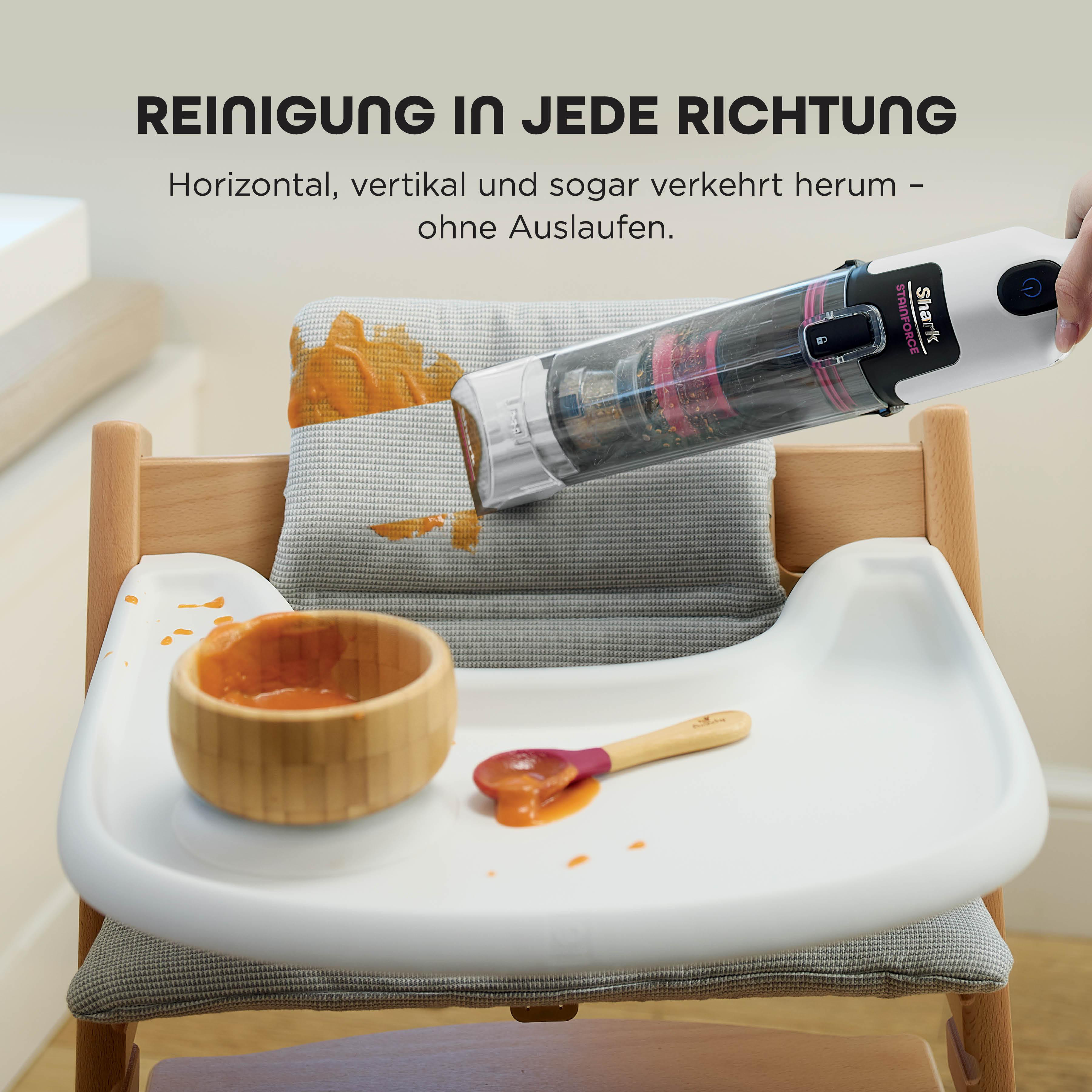 Ein Hochstuhl mit Essensflecken wird von einem Shark Stainforce Staubsauger gereinigt. Eine Schüssel, ein Löffel und Essen sind sichtbar.