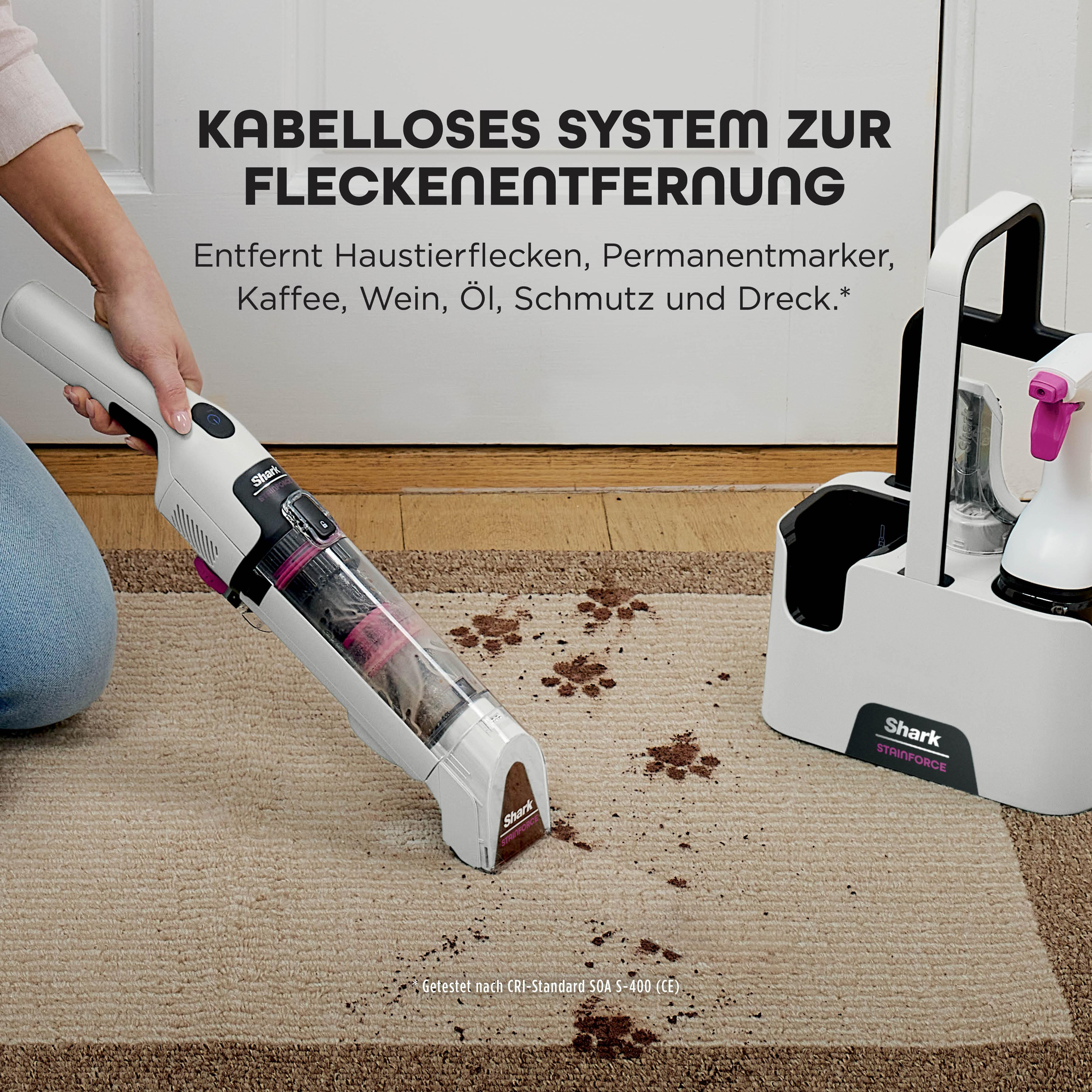 Eine Frau benutzt einen Shark Stainforce Staubsauger auf einem Teppich mit Flecken. Rechts ist ein Reinigungswagen.