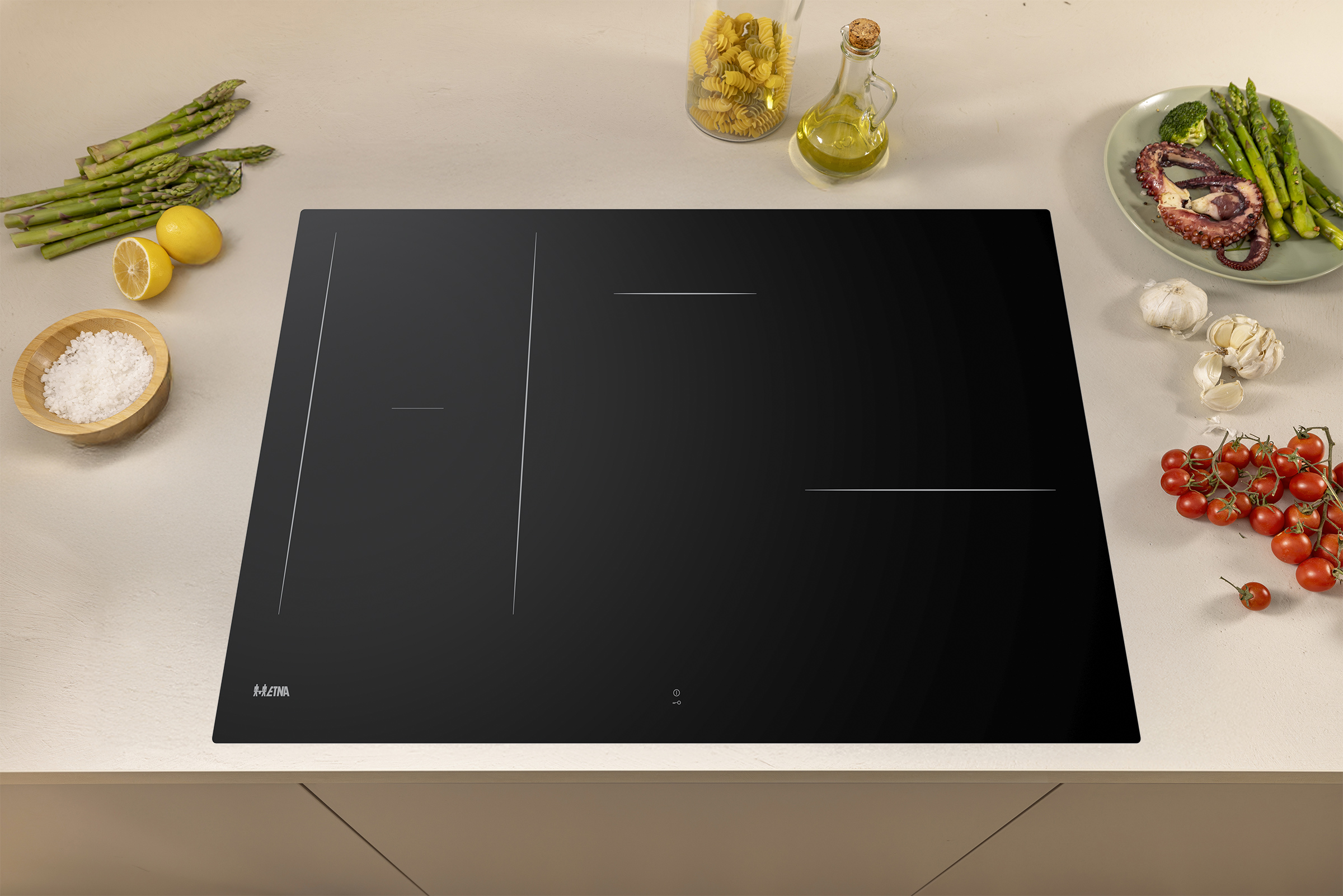 A black induction cooktop with food ingredients like asparagus, tomatoes, and pasta.