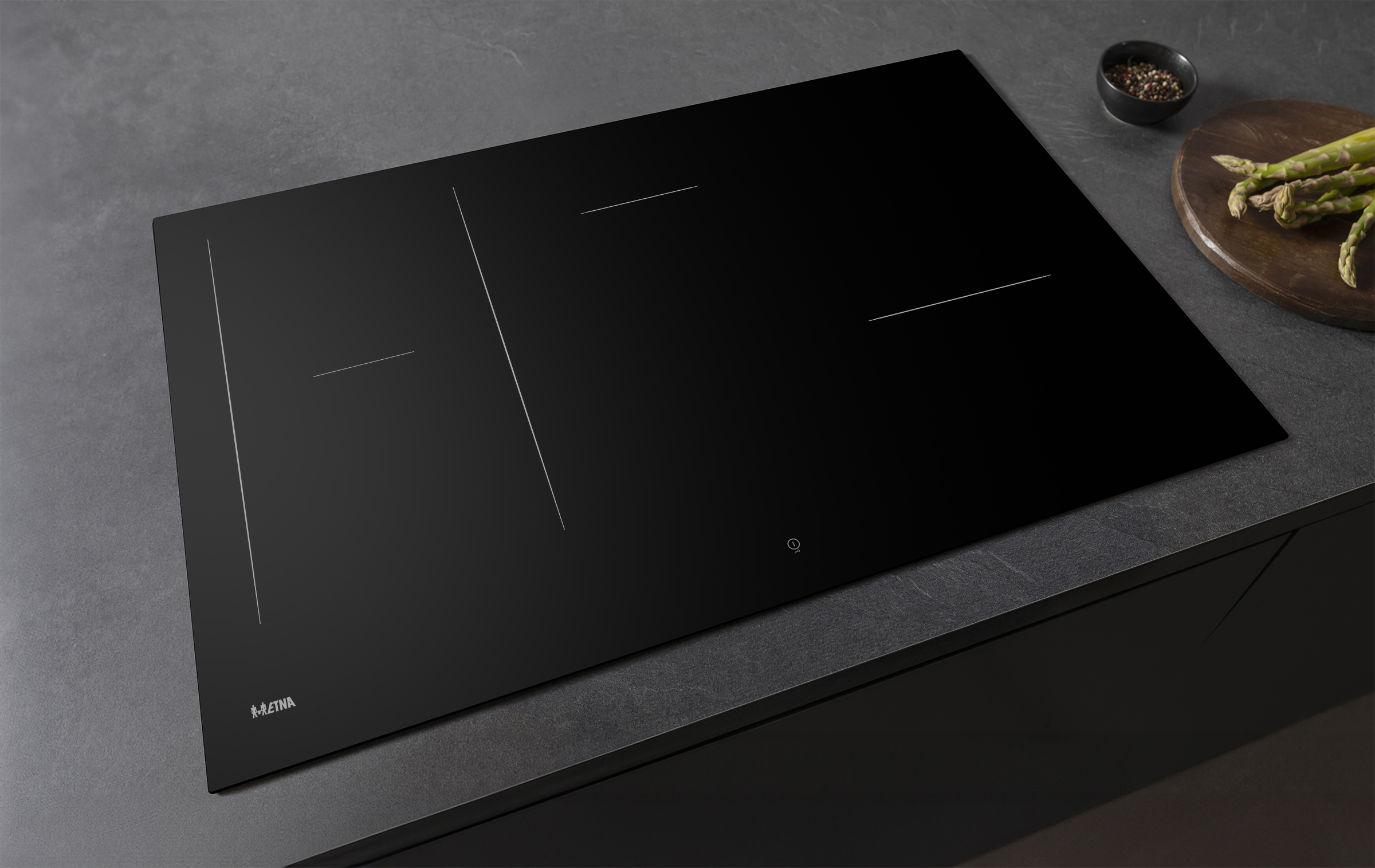 Black induction cooktop with white lines. Asparagus, spices, and a wooden board are on the side.