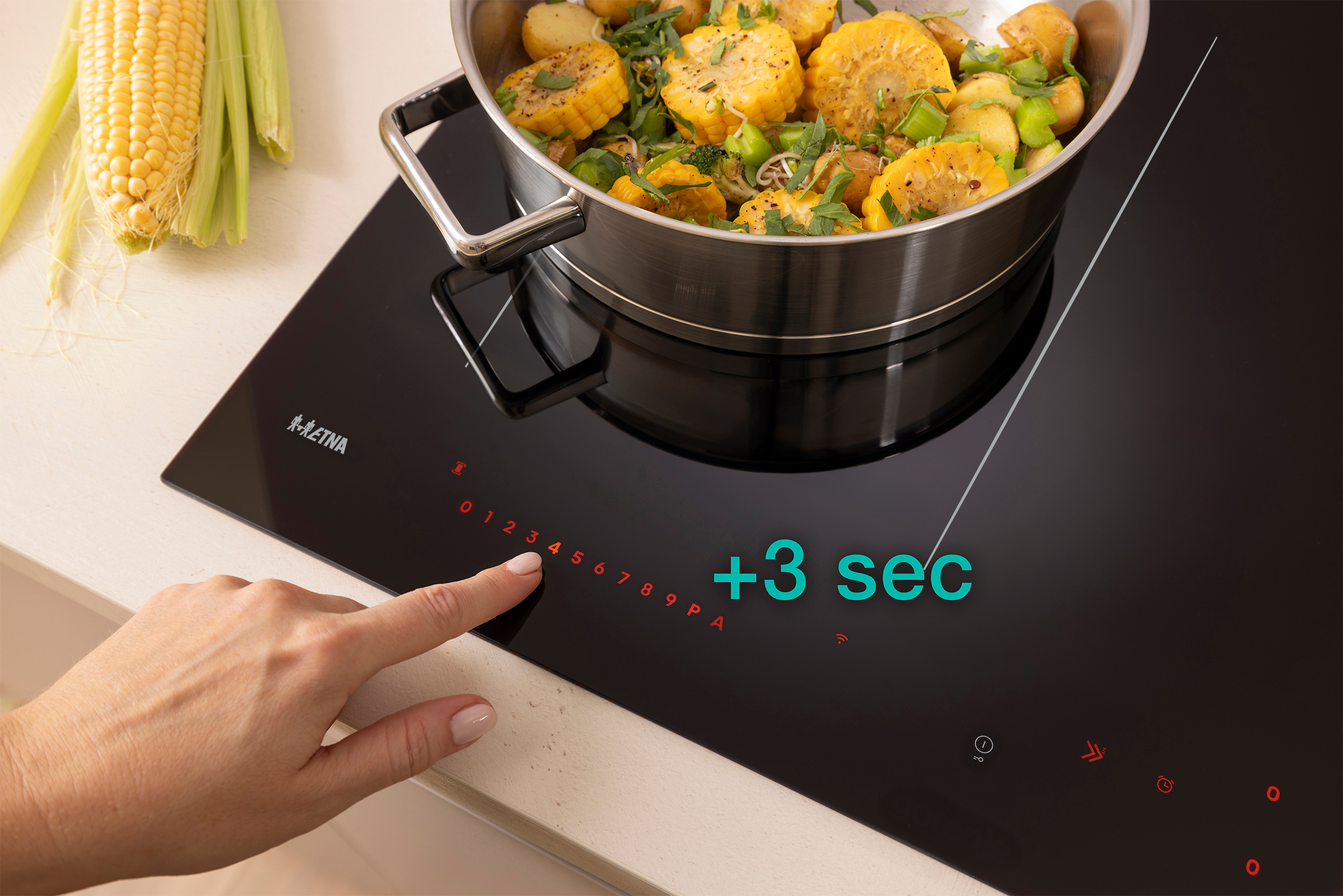 A hand touches the 4 on a black stove. A pot of food simmers on the stove. Corn is on the counter.