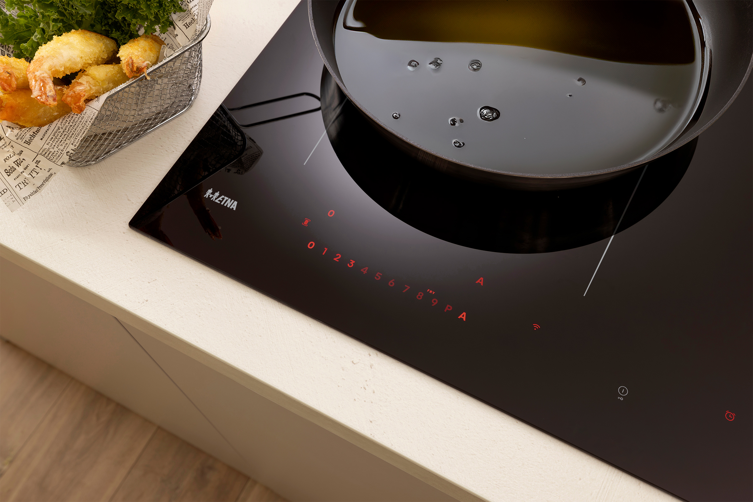 A black induction cooktop with a pan of oil and fried shrimp in a basket are on a white countertop.