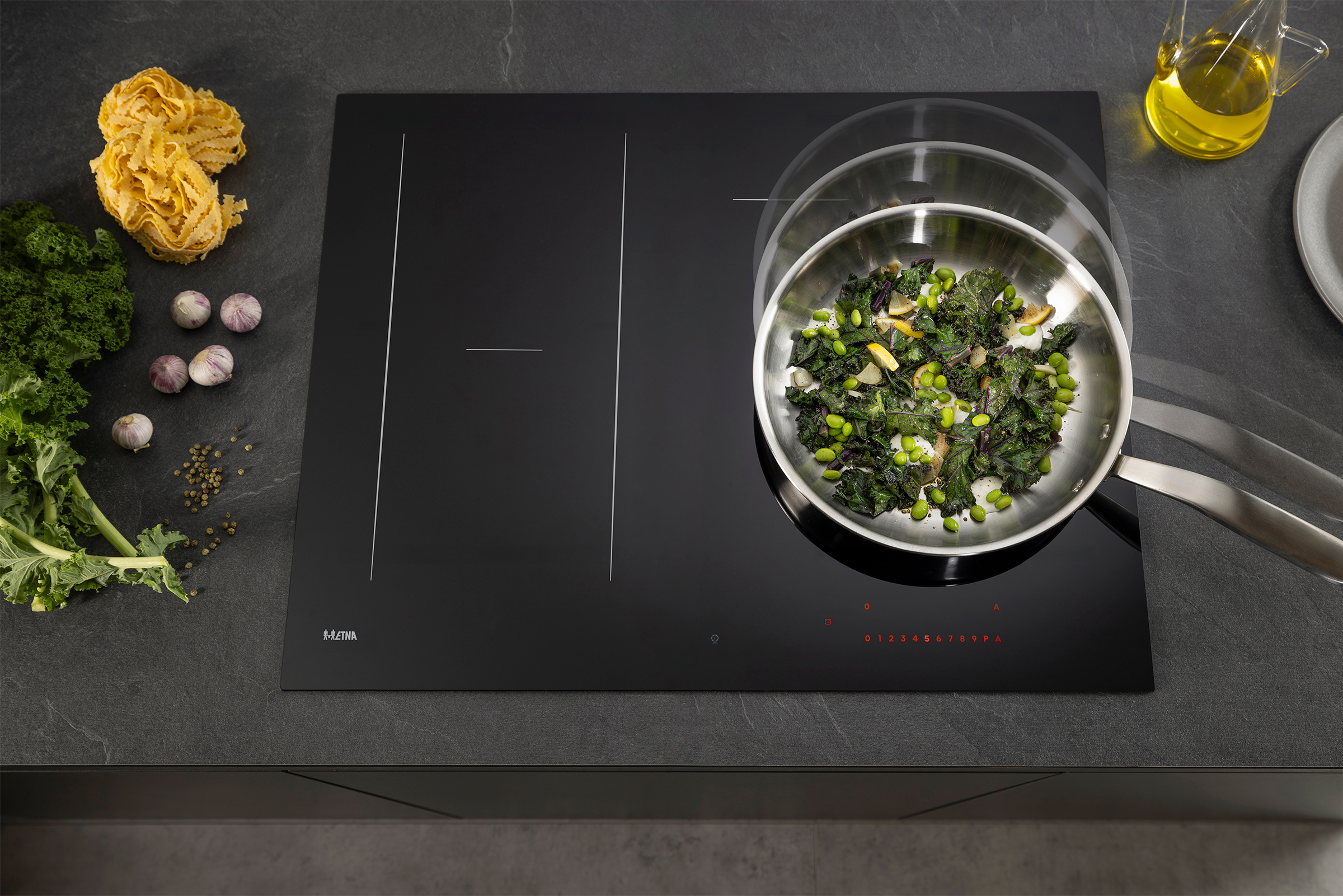 A black induction cooktop with a pan of food, pasta, garlic, and oil.