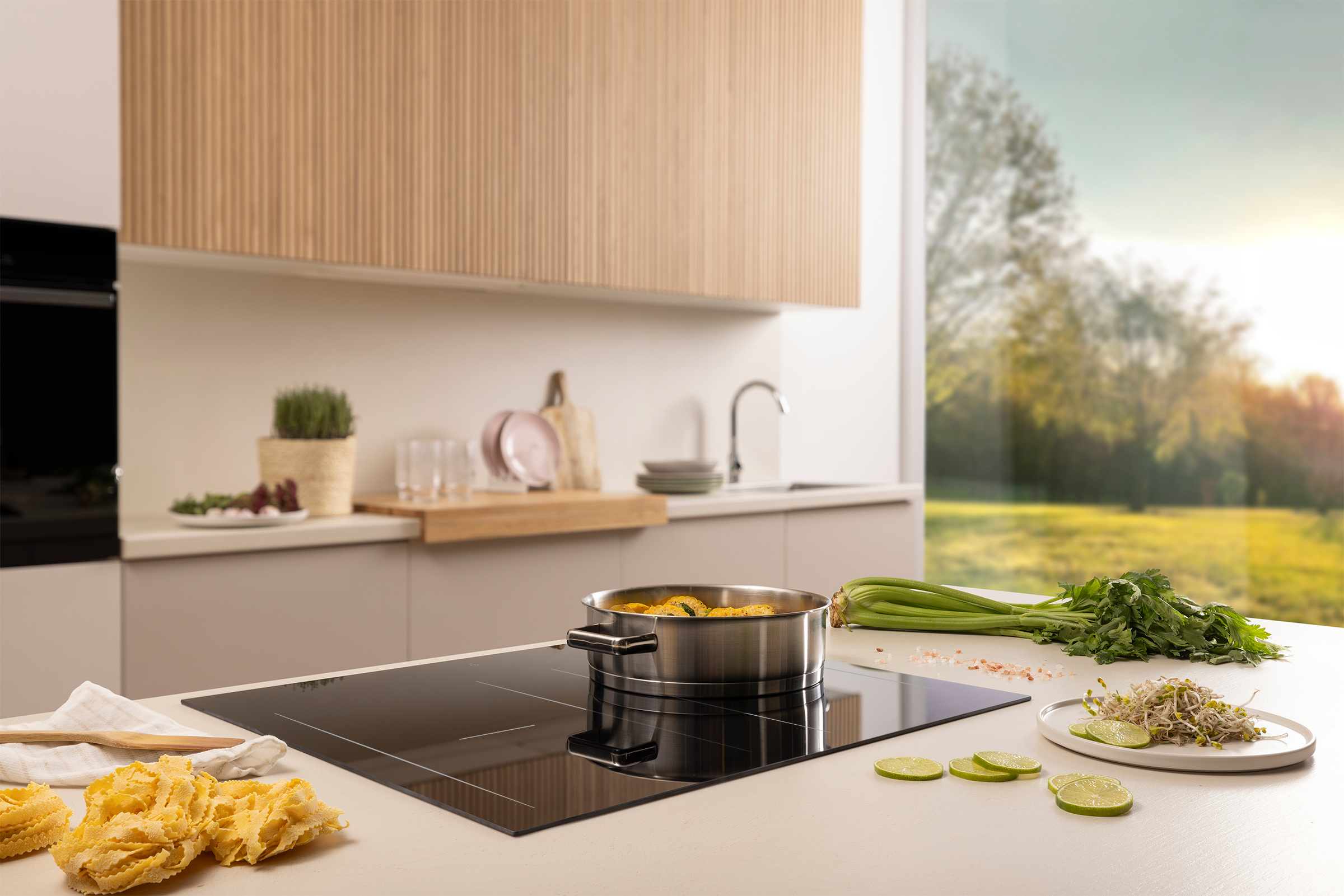 Kitchen scene. Pan with food on a stove. Pasta, vegetables, and a window with a blurry outdoor view are visible.