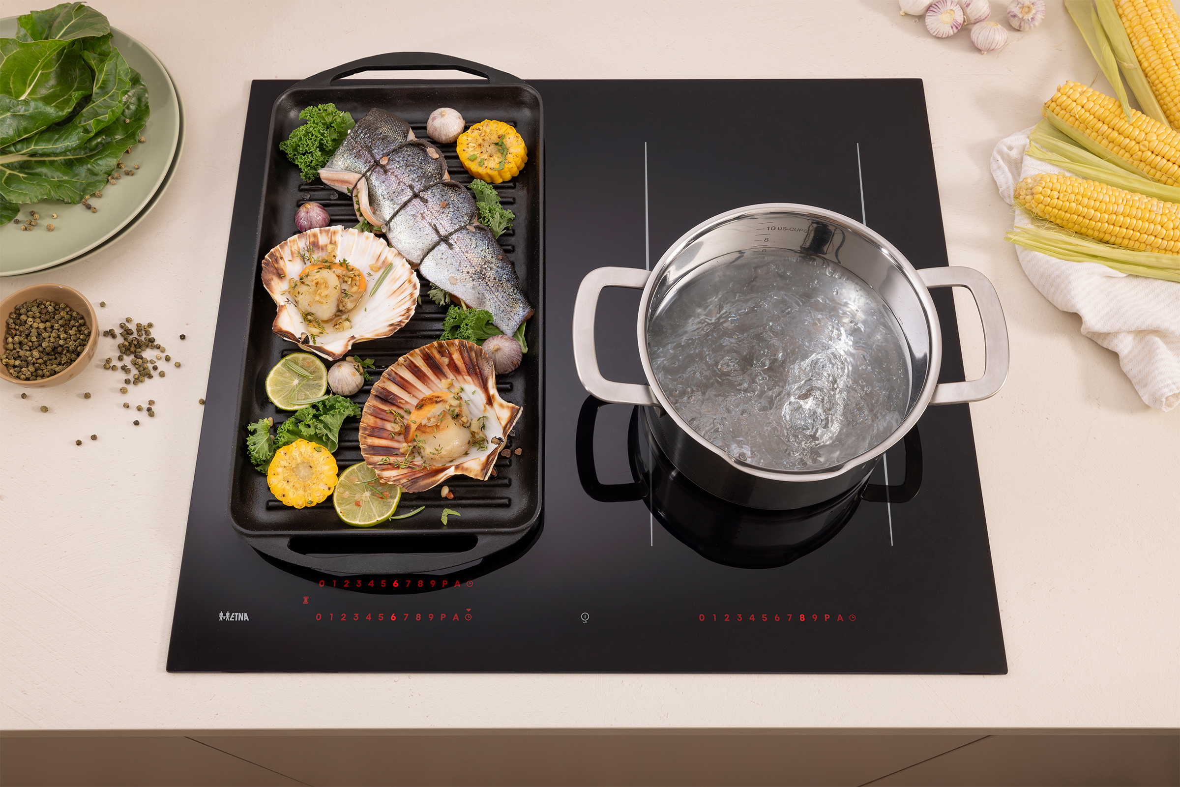 Seafood on grill with corn and pot on stove. Green leaves and bowl with spices are also present.