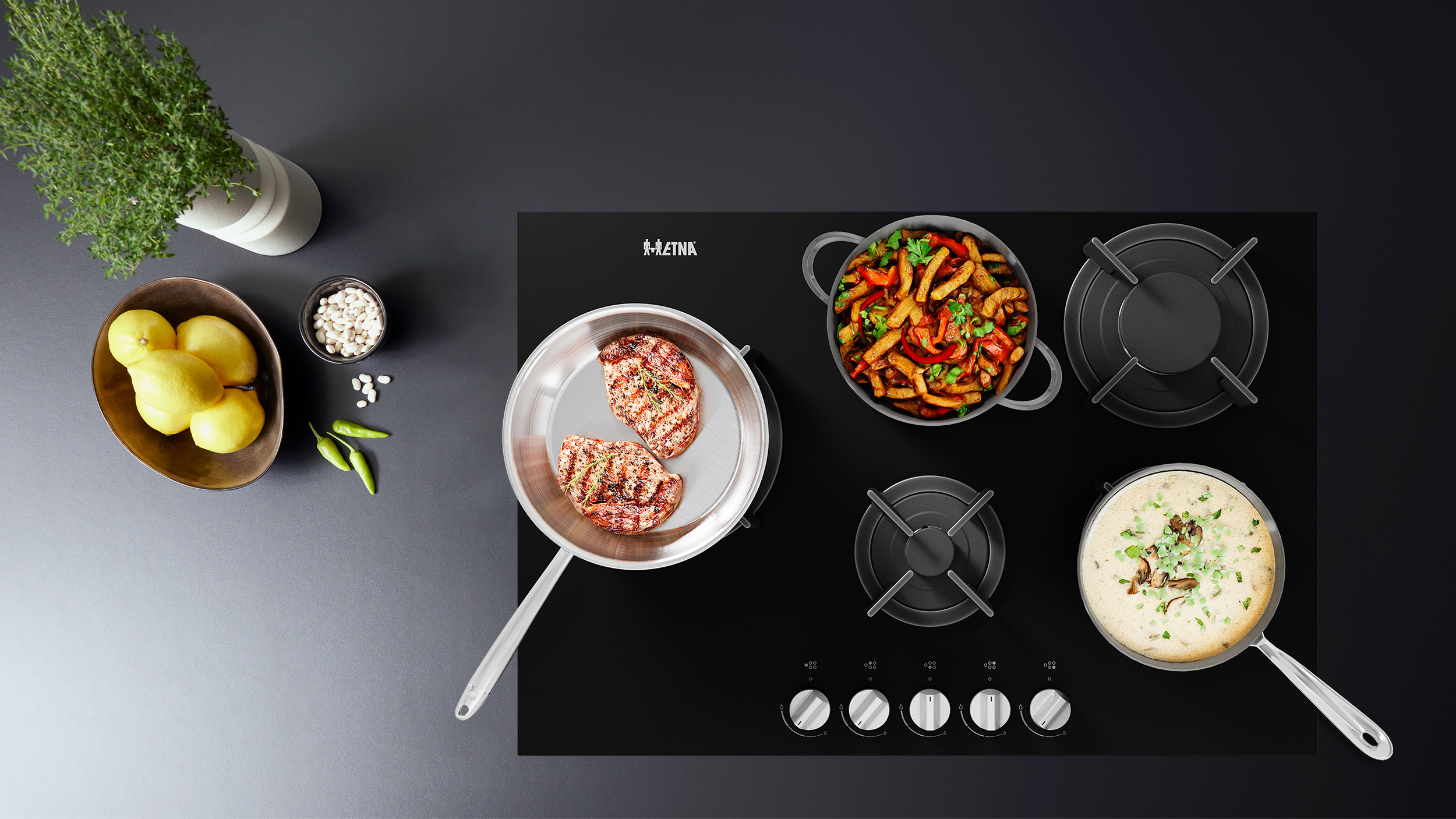Overhead shot of a black stovetop with pans of food, lemons, beans, and herbs. Steaks are grilling in one pan.